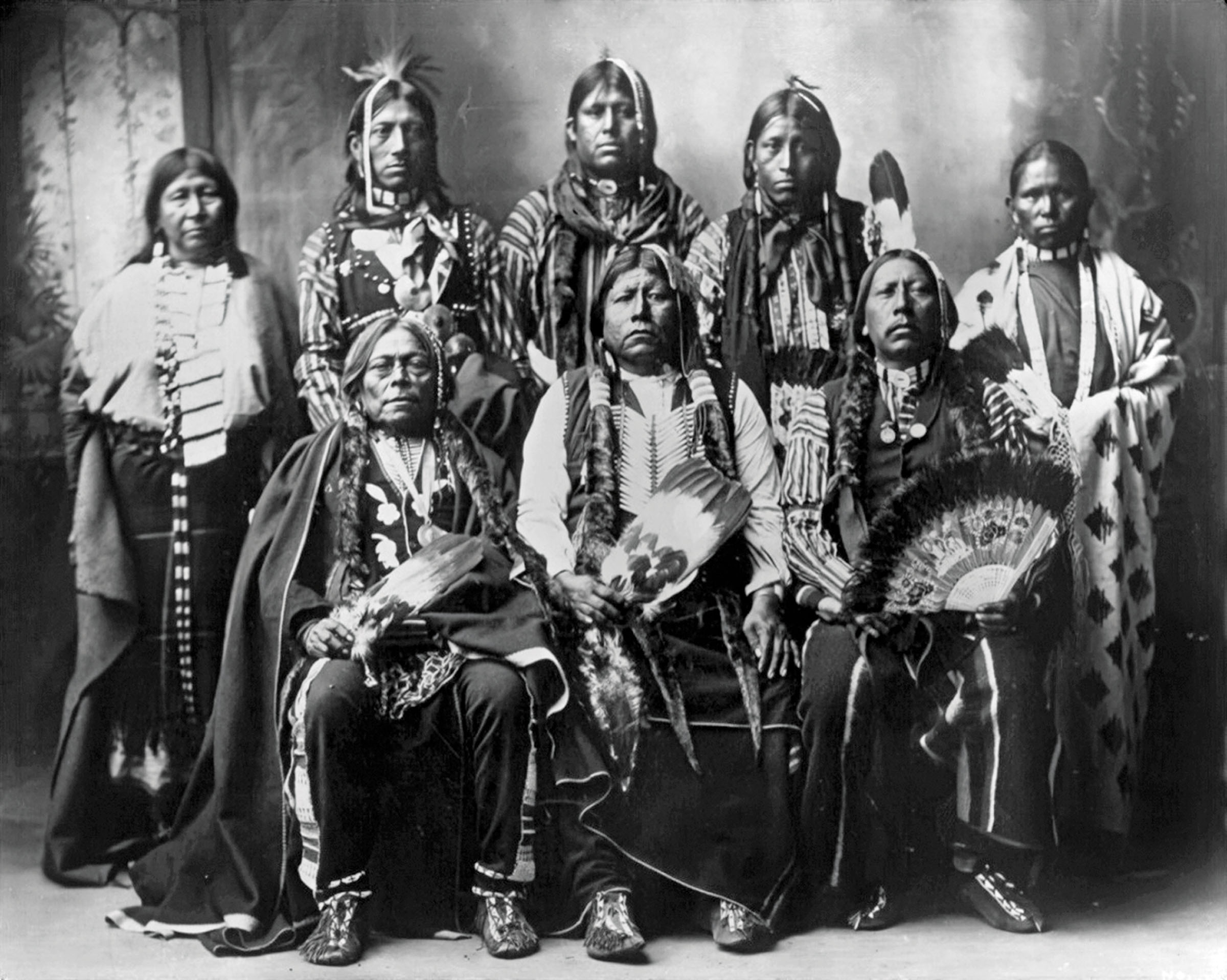 A black and white photograph of a group of Native Americans wearing traditional attire 