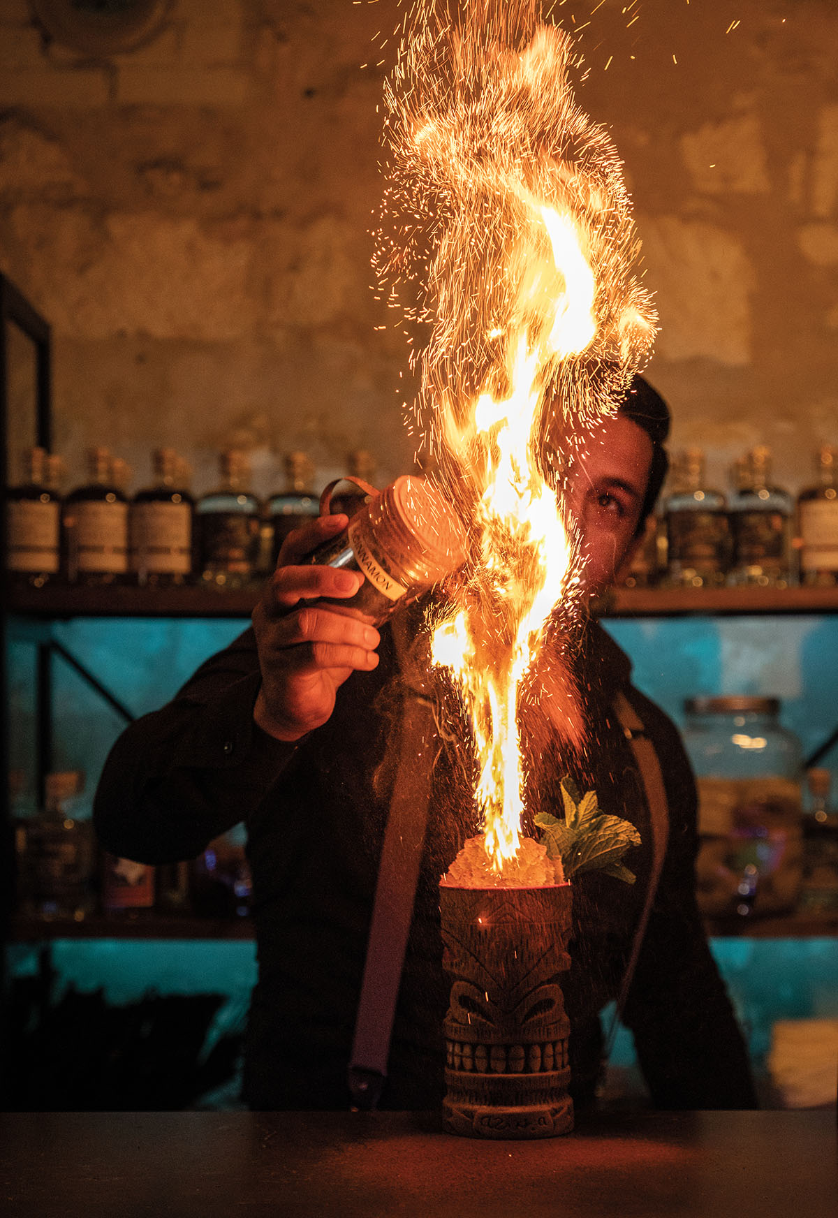 A bartender stands back as a large column of fire and sparks shoots up from a cocktail