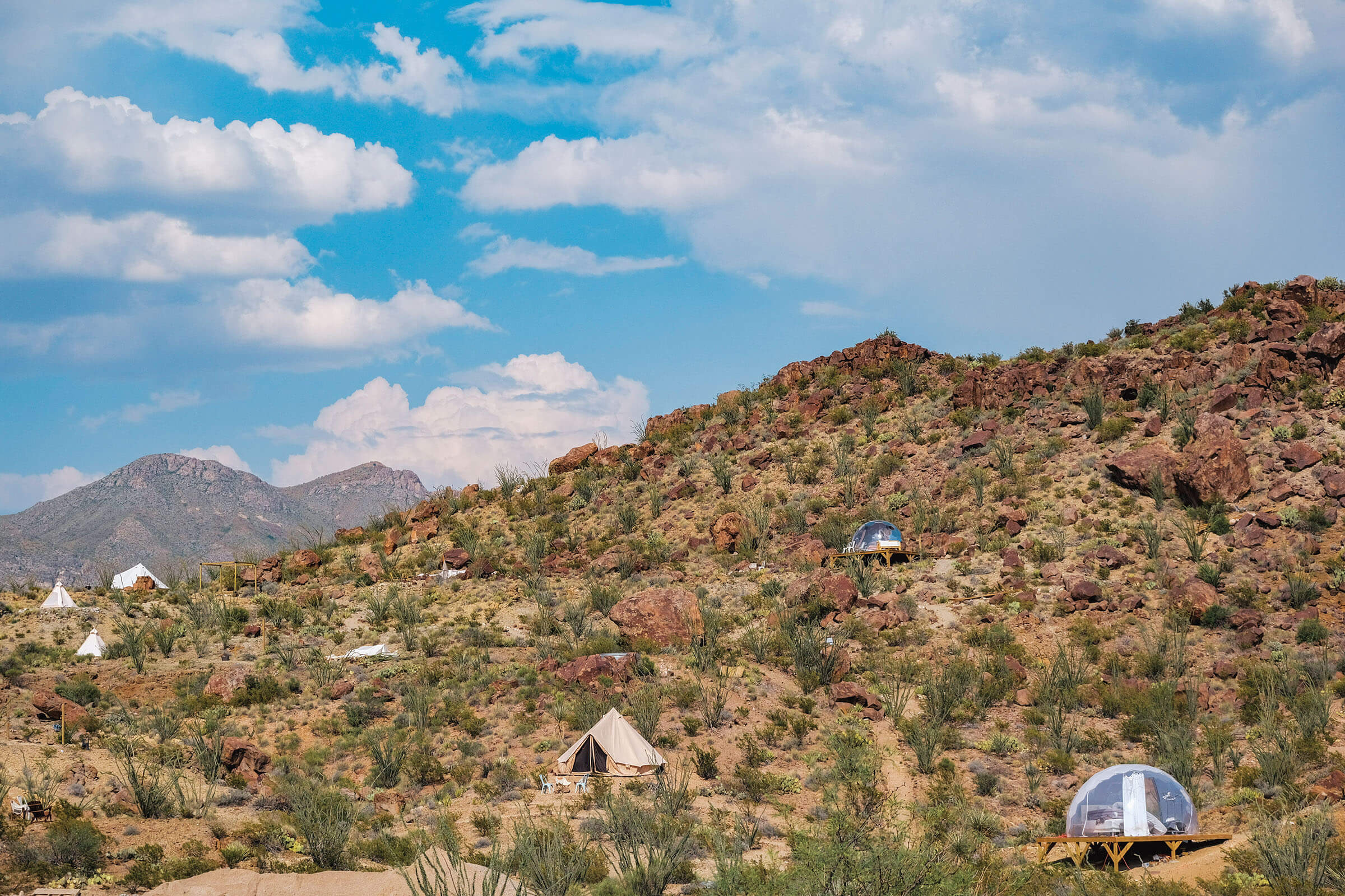 Clear 'bubble' style lodging dots a desert hillside under blue sky