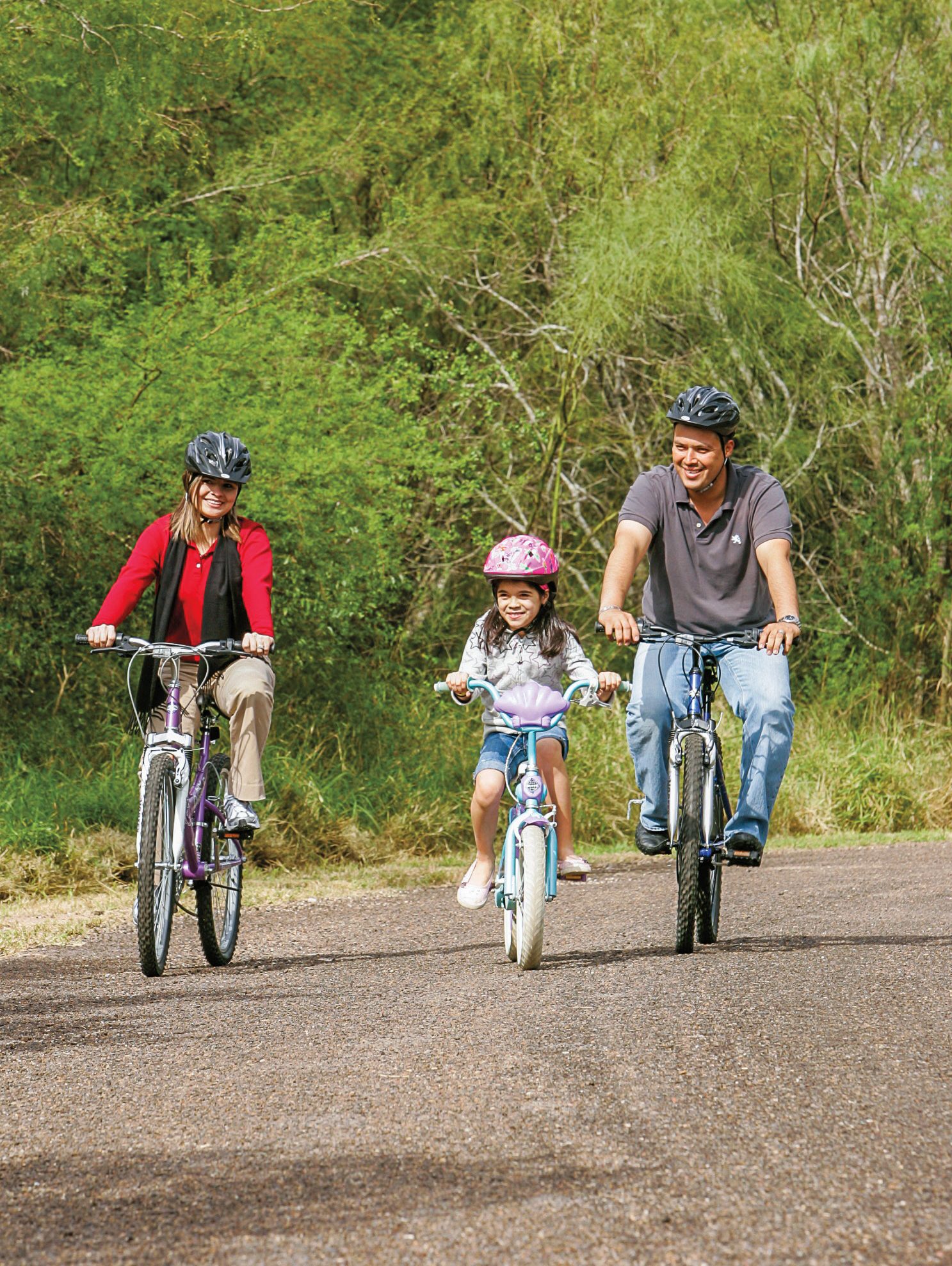 Two adults and a child ride bikes on a gravel road.