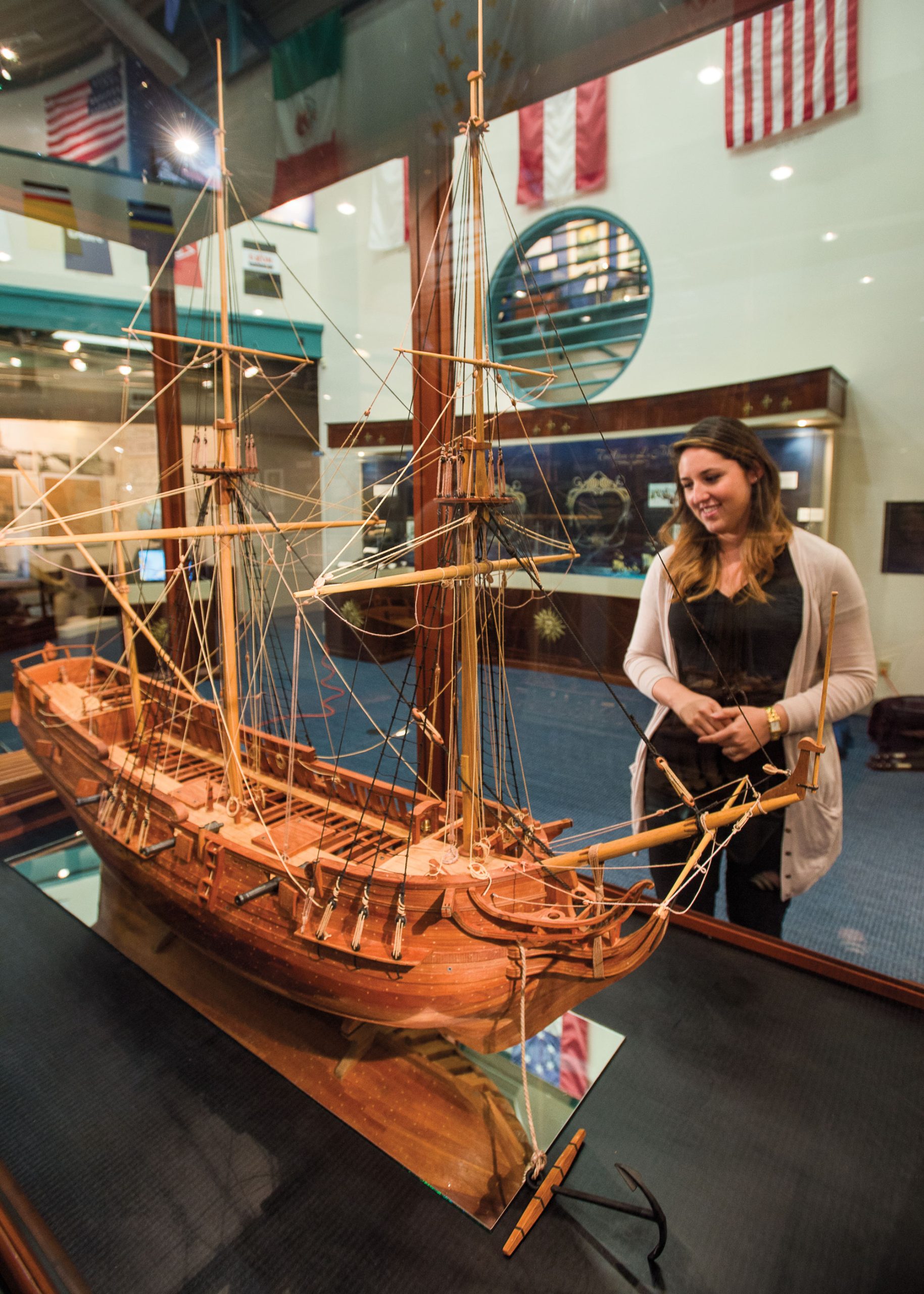 A woman looks at a wooden replica of a ship on display behind glass.