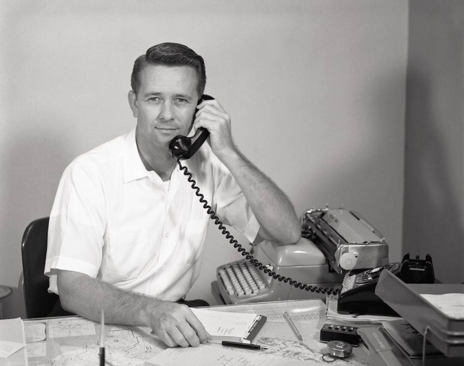 A black and white photograph of a man holding a telephone