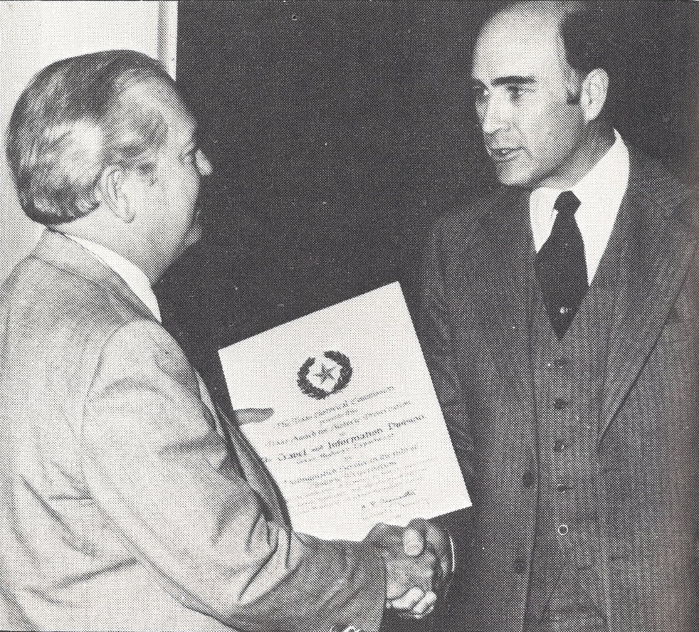Two men shake hands as one receives an award