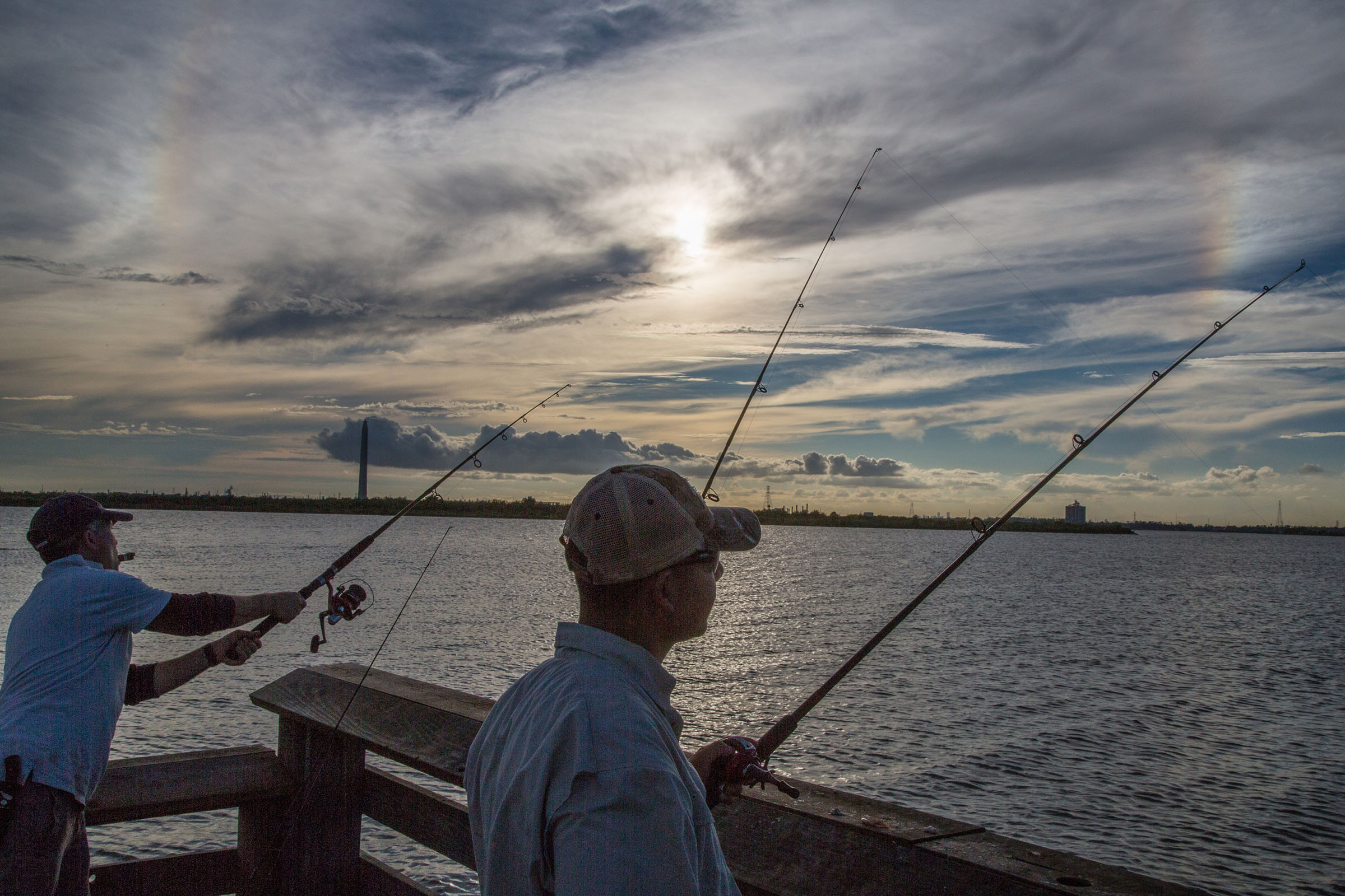 Man fishing off a pier on a sunny, partially cloudy day