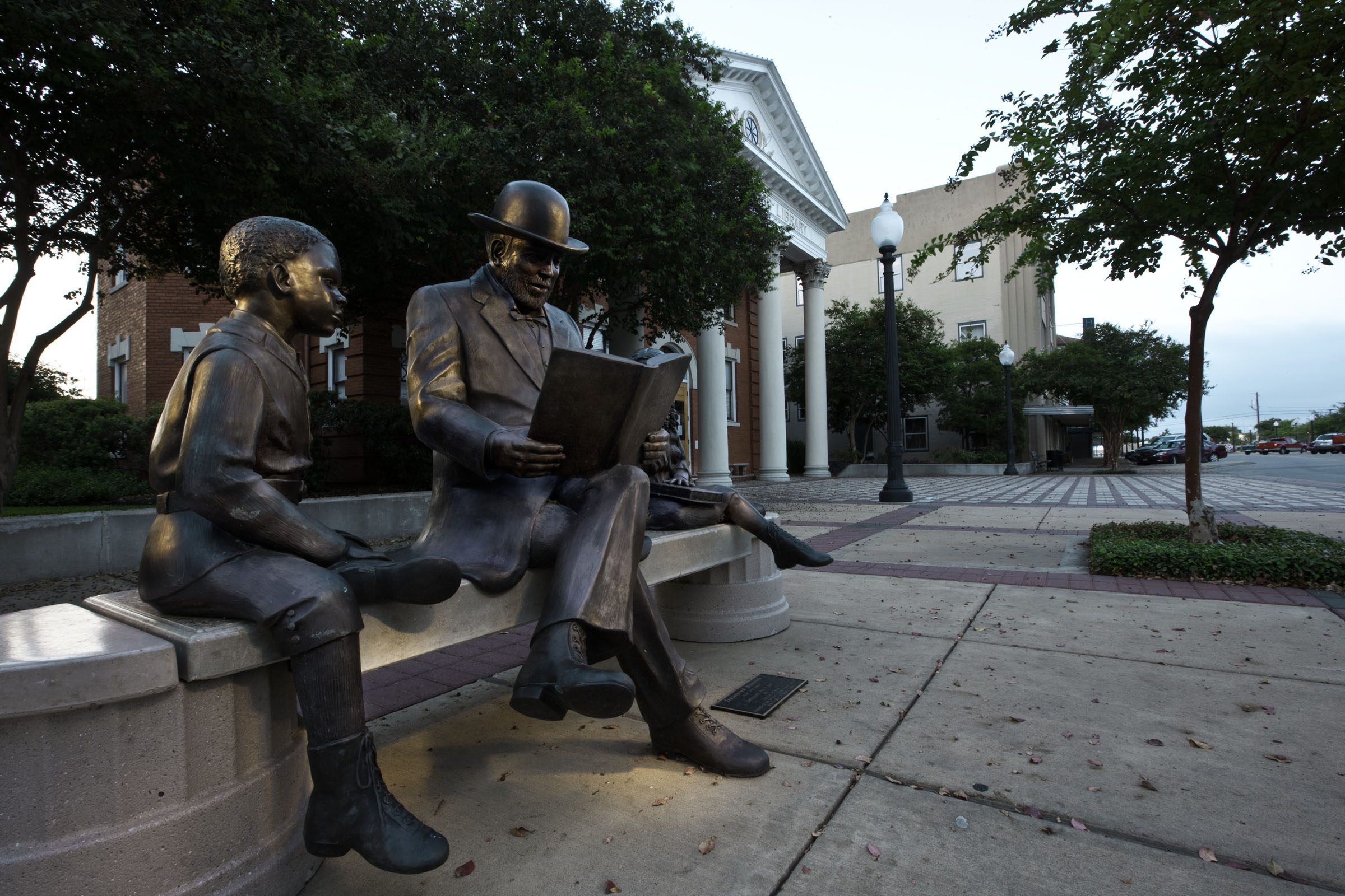 A bronze statue of a man reading a book to a child while sitting on a bench.