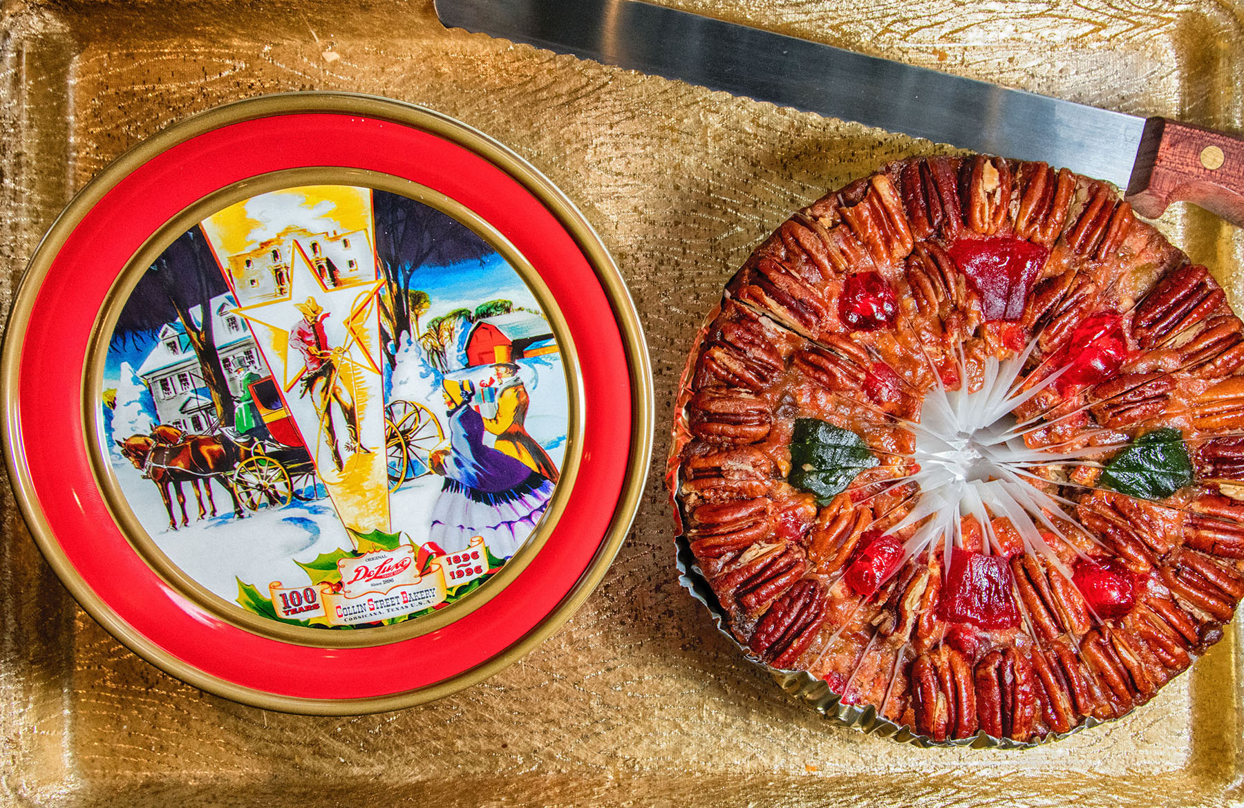 A fruit cake sitting next to a decorative tin on a wood countertoop
