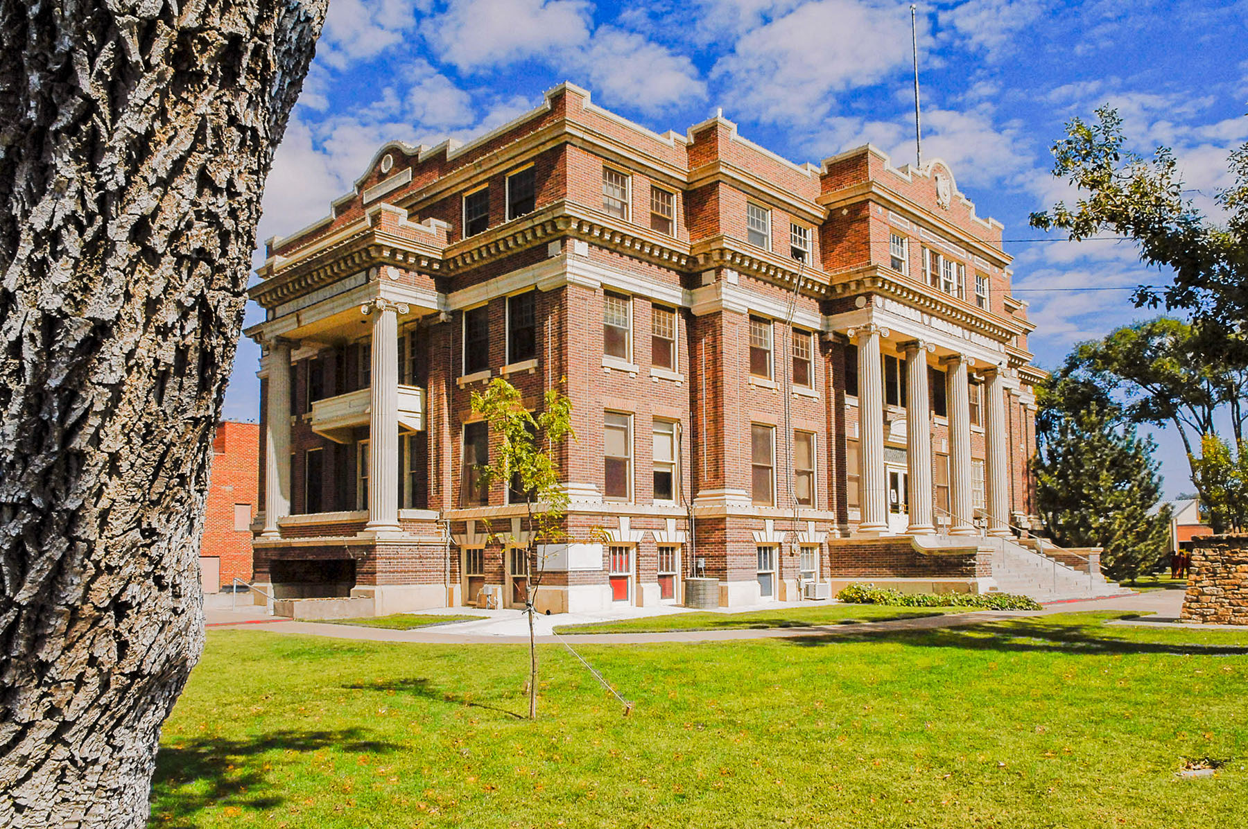 A large reddish-brown building with columns in front, surrounded by grass on a sunny day.