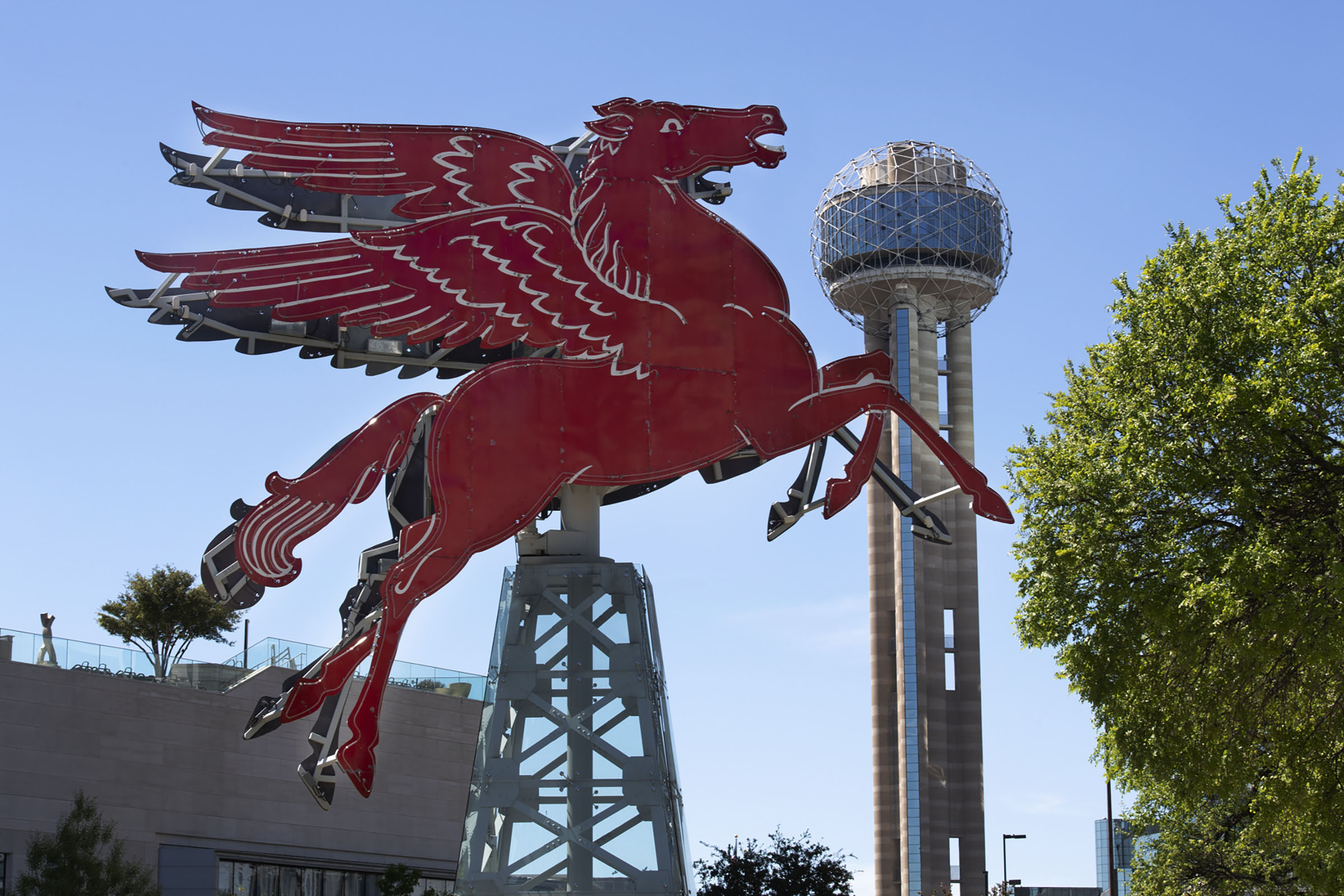 A red Pegasus sculpture flies in front of a large building with a spire