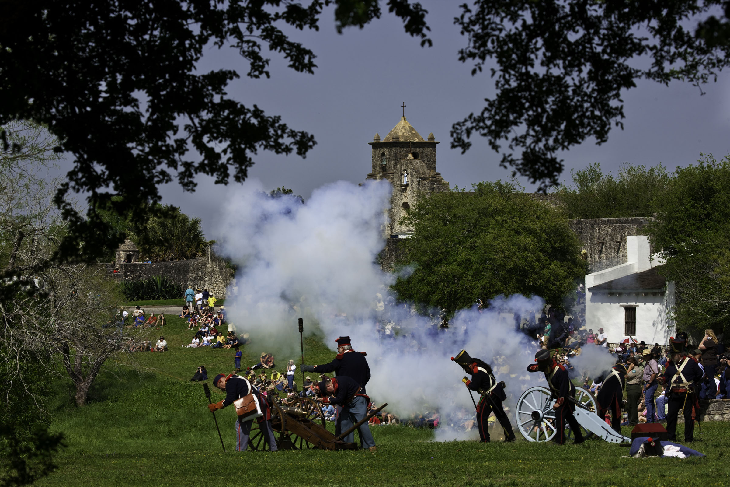 A war recreation on a grassy field. A cannon sends up a plume of white smoke as soldiers stand behind