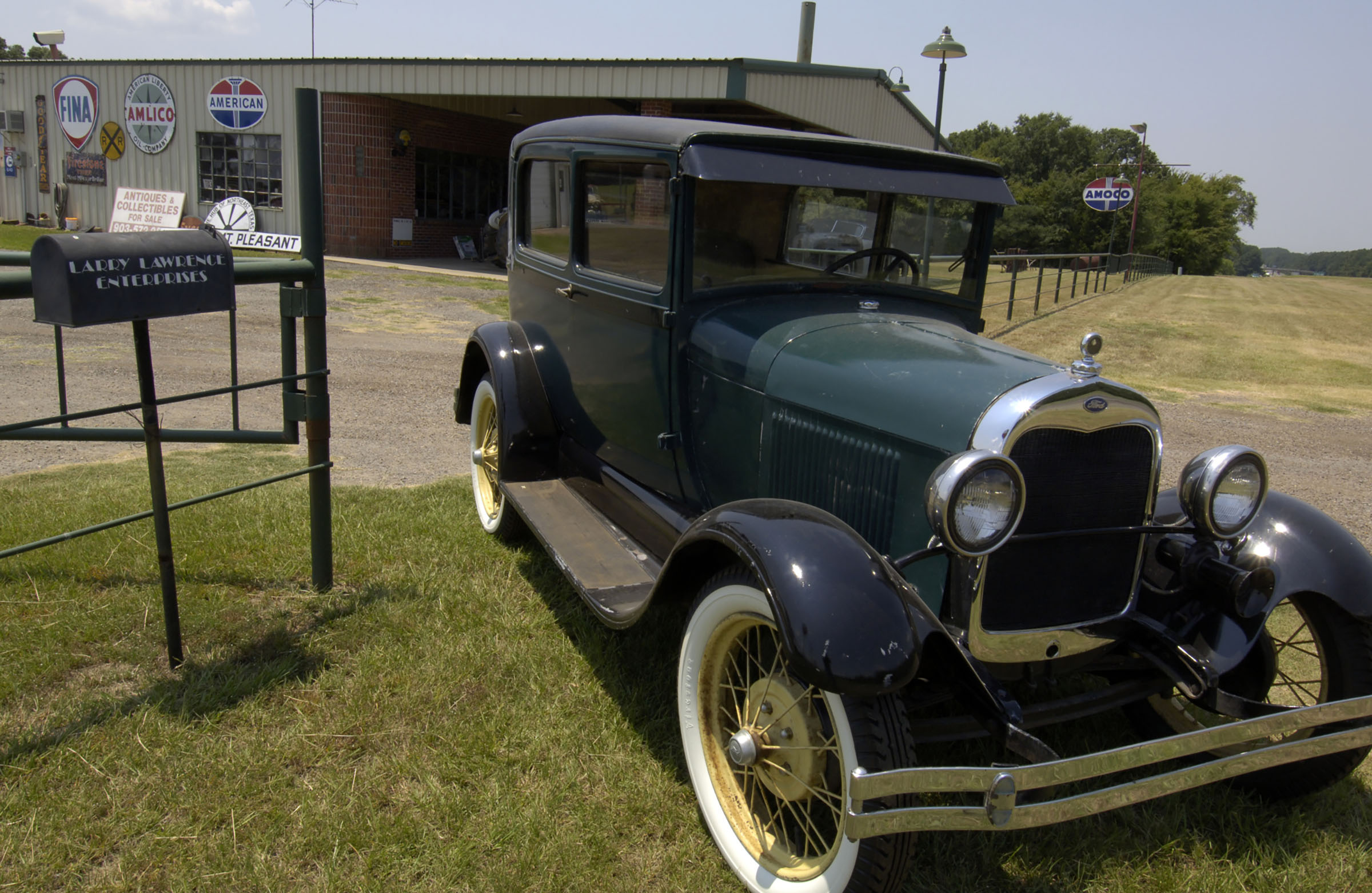 An antique car sits on a lawn in front of a small ranch style house.