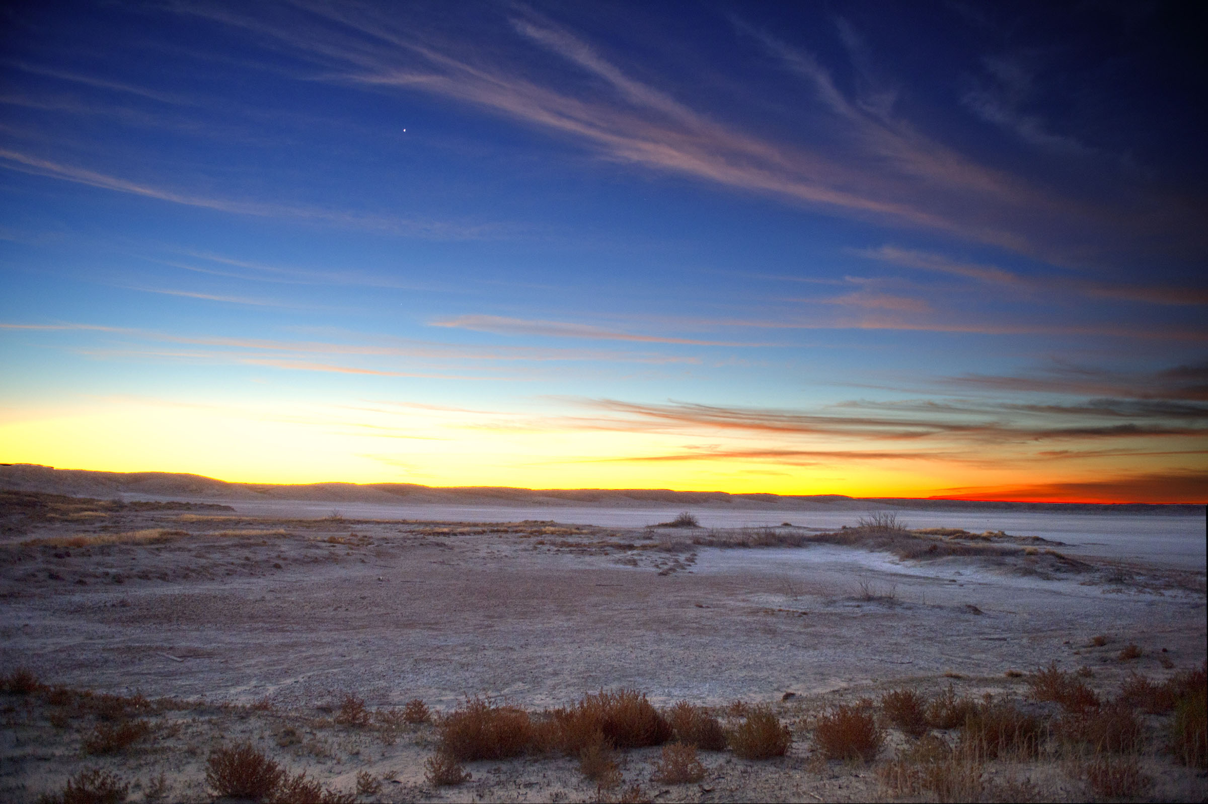 A sweeping desert landscape with a blue to orange sunset.