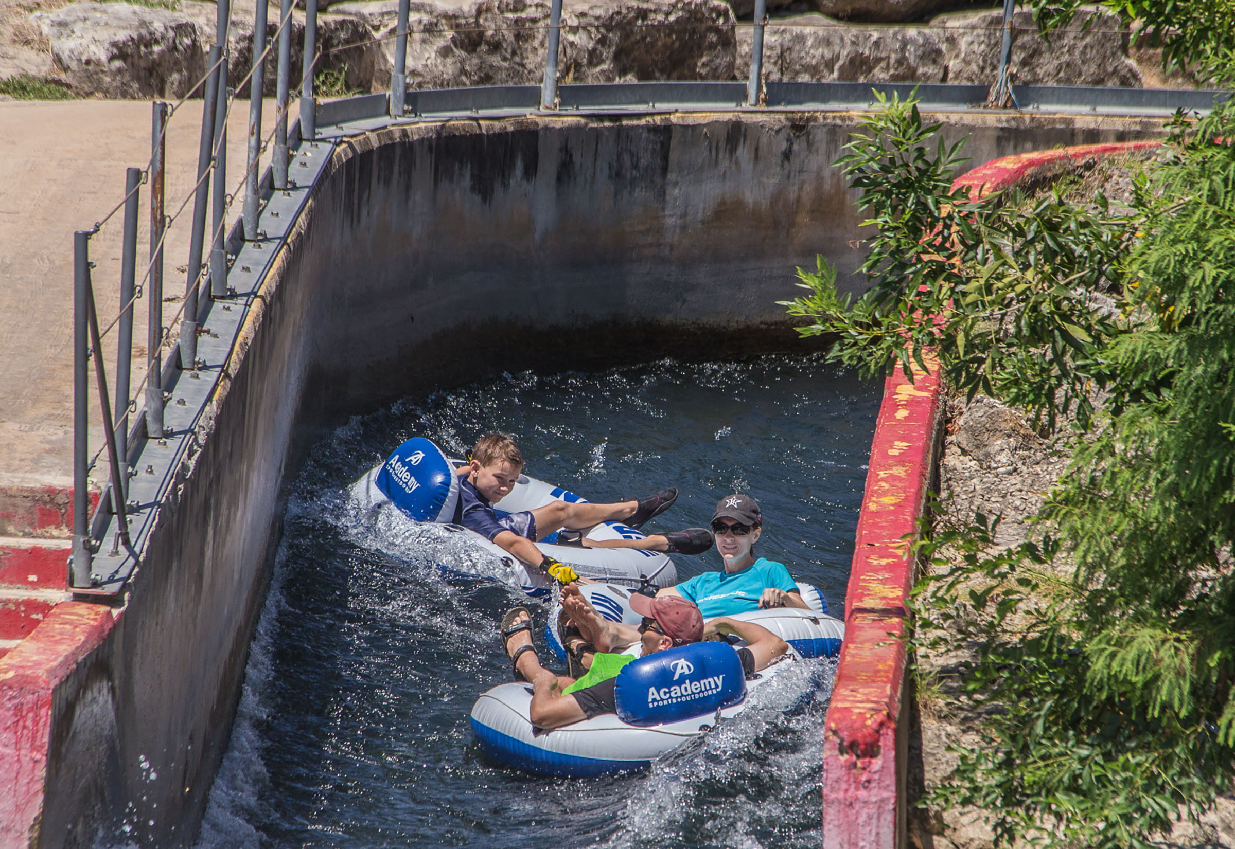 Three children float down a narrow canal on inflatable tubes.