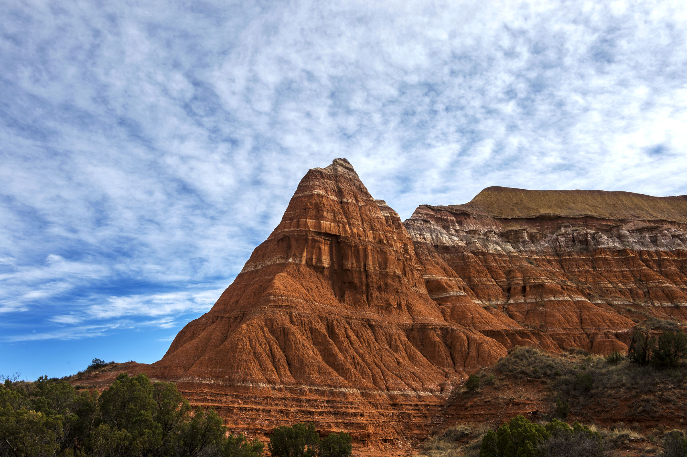 A large red rock outcropping against a semi-cloudy blue sky