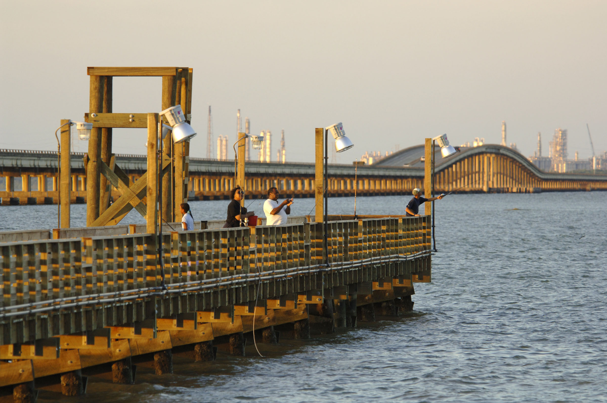 Three people fish off of a wooden pier at sunset.