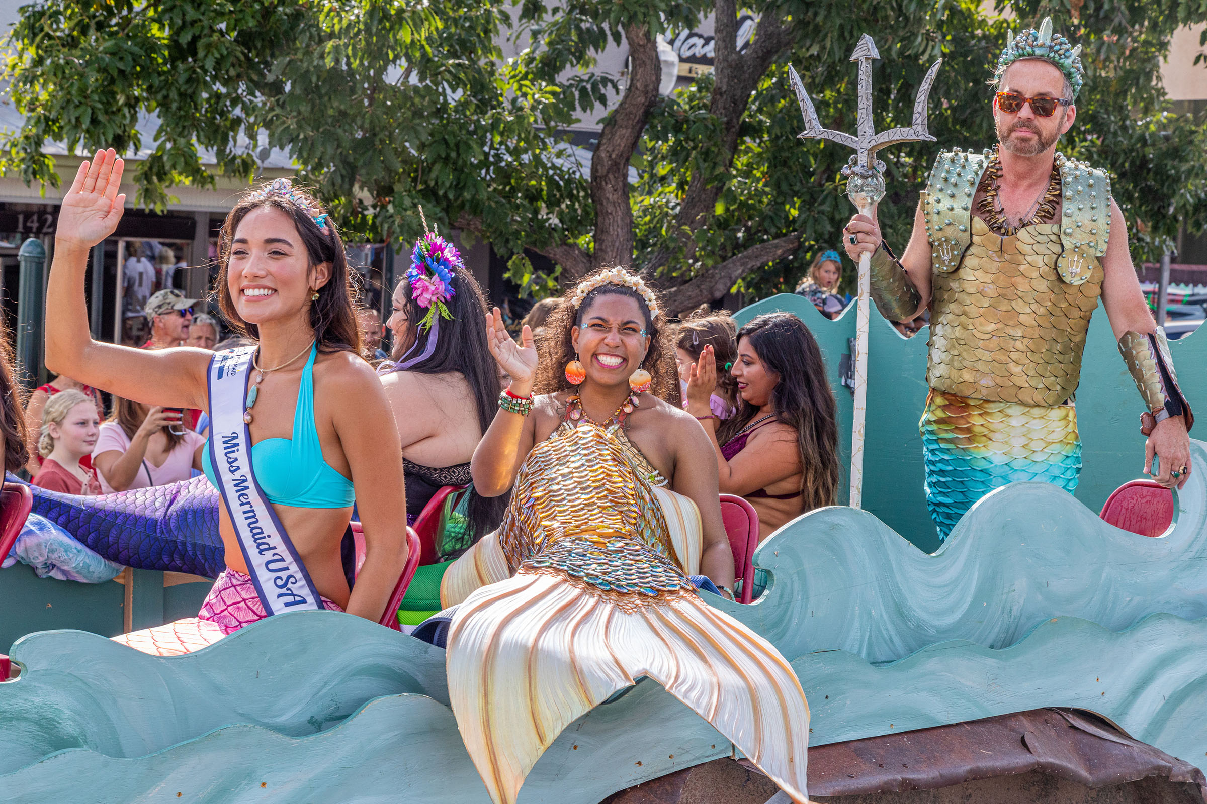A group of men and women in mermaid costumes pose on a parade float