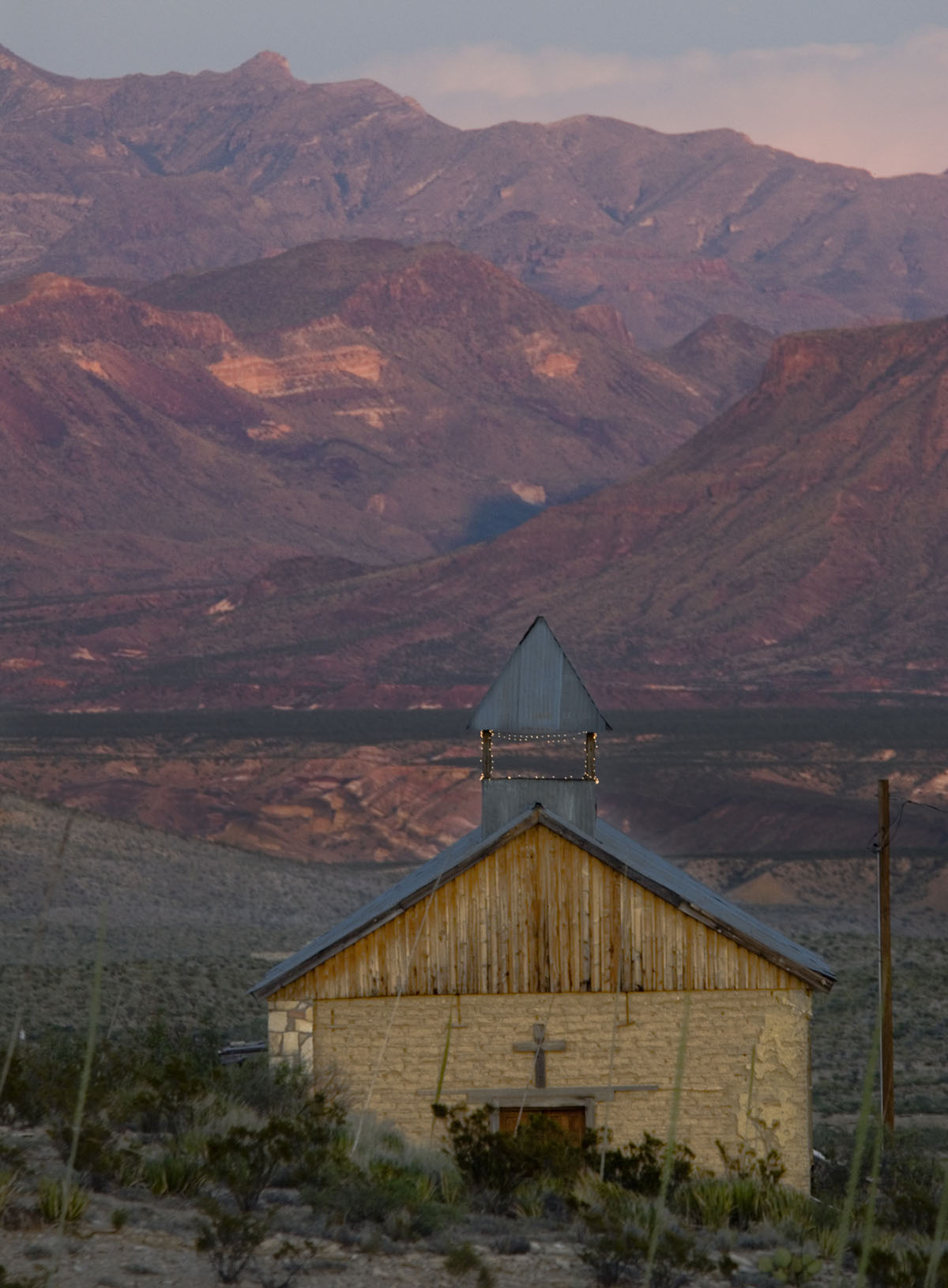 A small abandoned church sits at the base of sweeping red and brown rock mountains