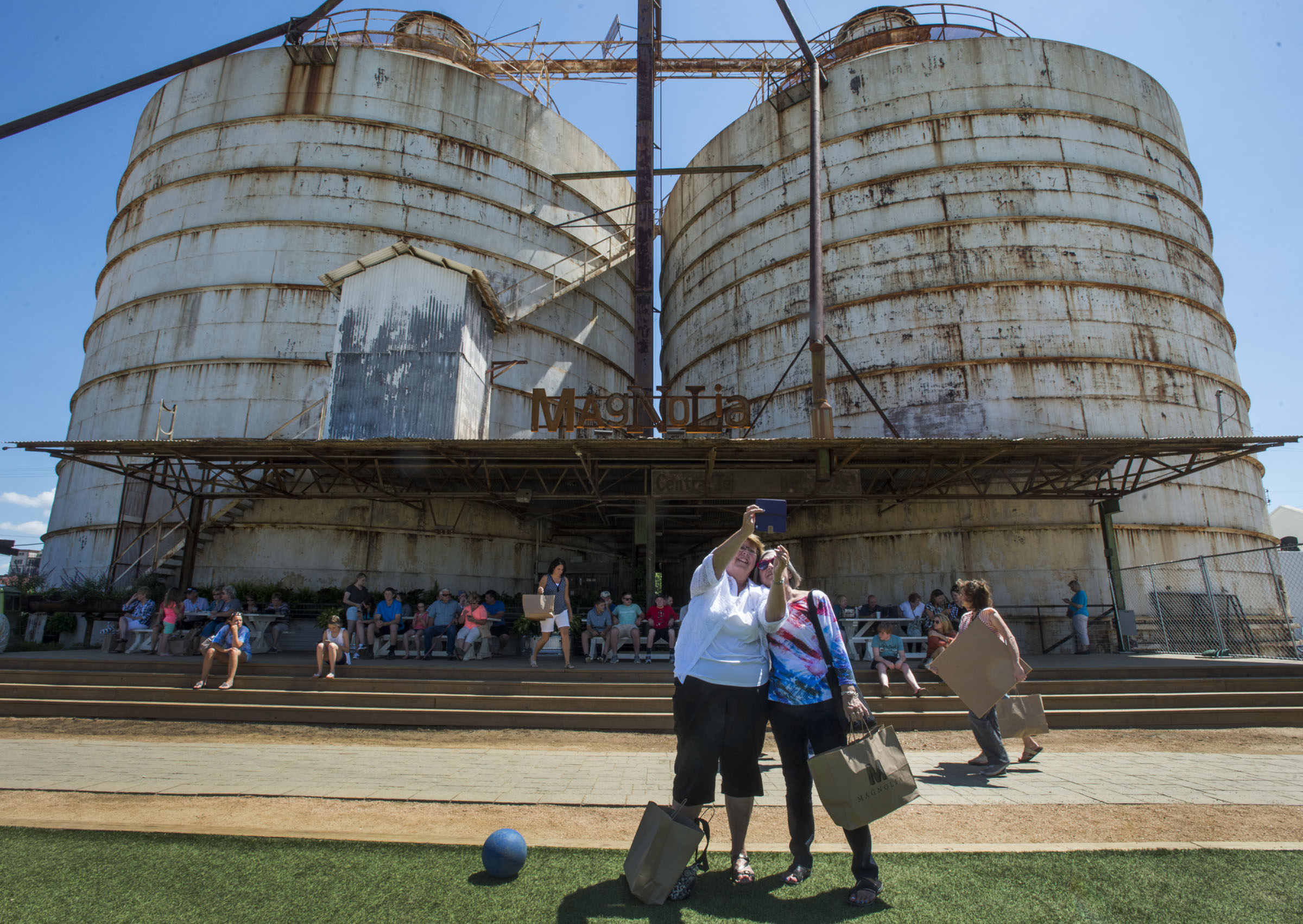 Two people take a selfie in front of large metal grain silos