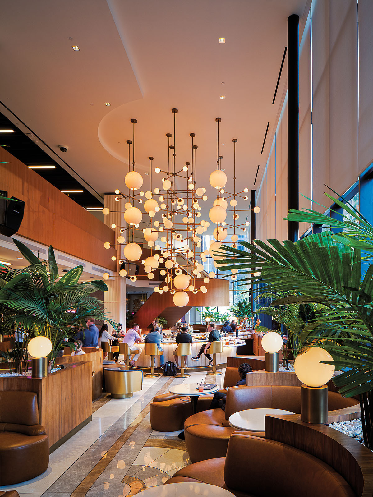 Large globe pendant lights hang from the ceiling of a hotel lobby with large green plants