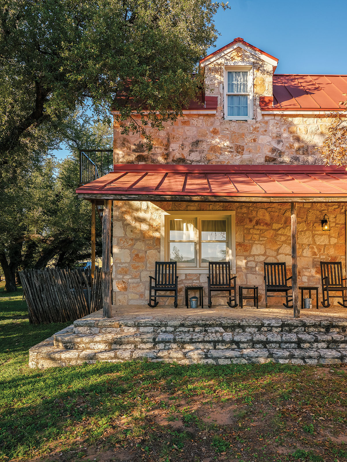 The exterior of a stone building with chairs on a porch