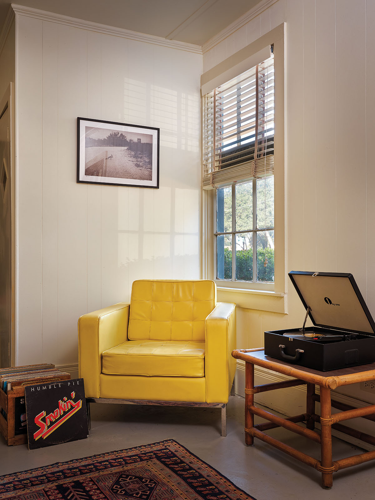A bright yellow chair is the focal point of a room with bright natural light and a record player