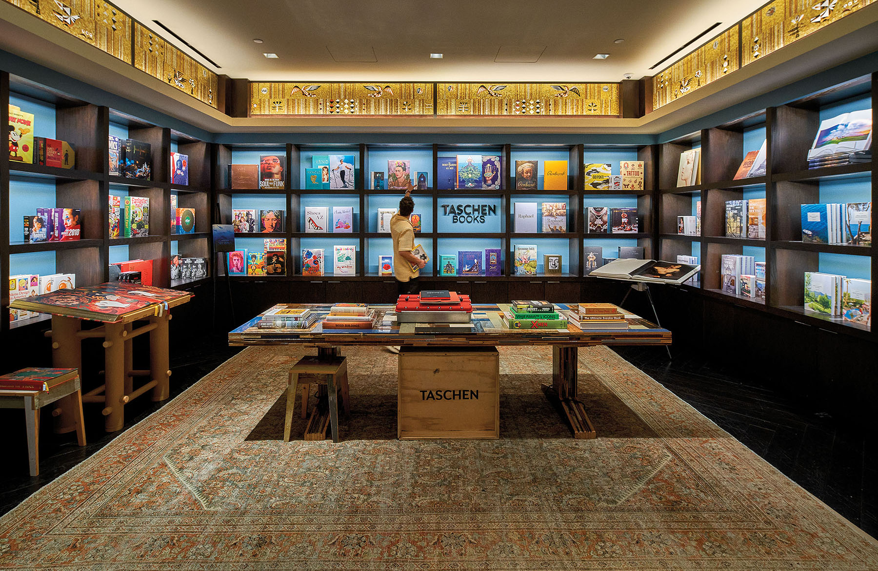 A warmly lit room with numerous shelves full of books and a small sign reading "Taschen Books"