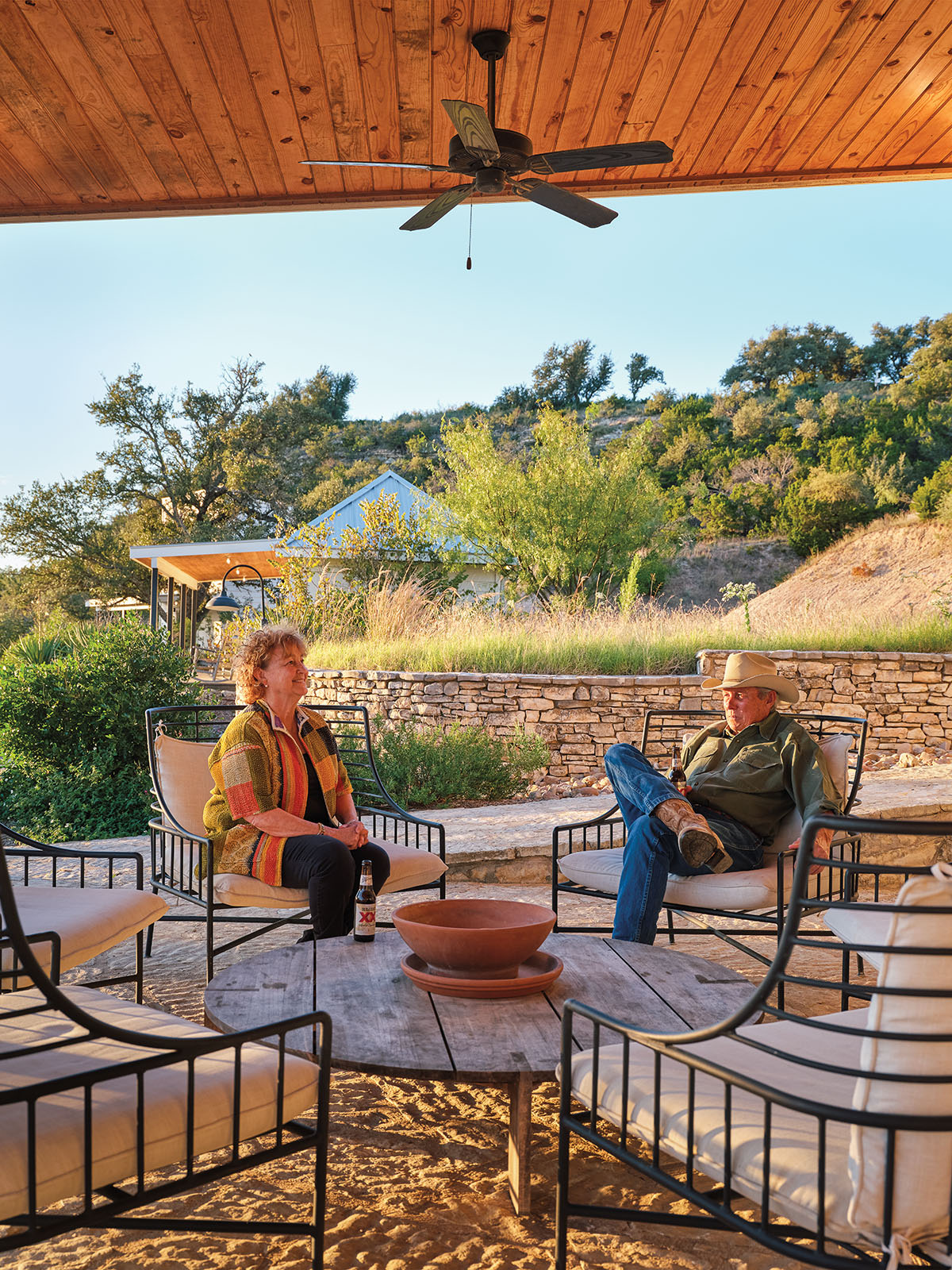 Two people sit in outdoor furniture around a stone firepit