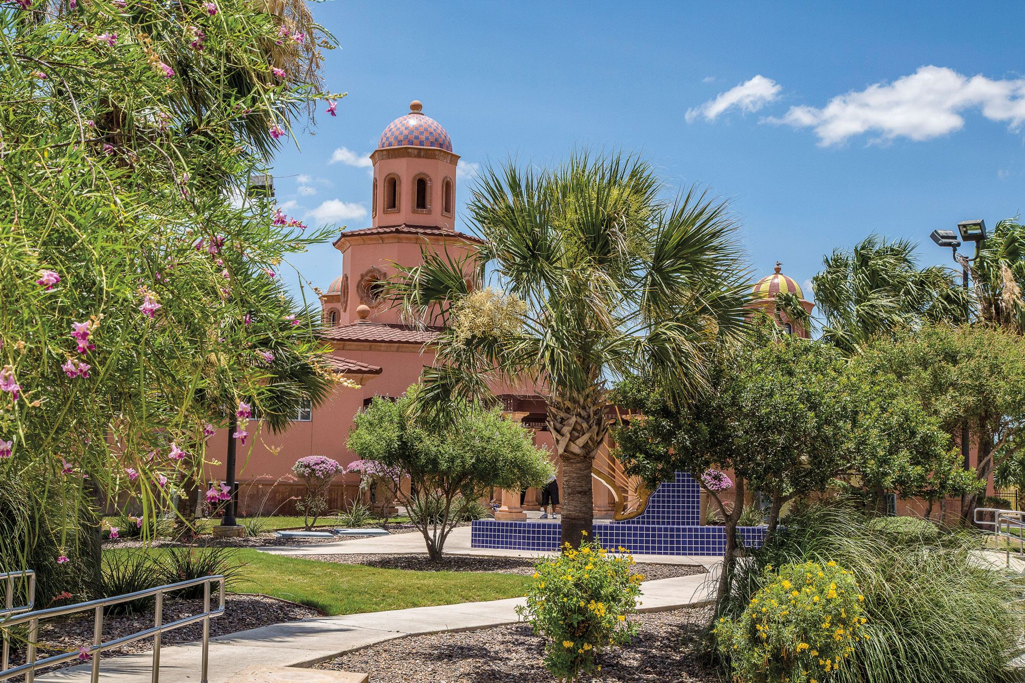 a clay-colored building foregrounded by palm and other trees
