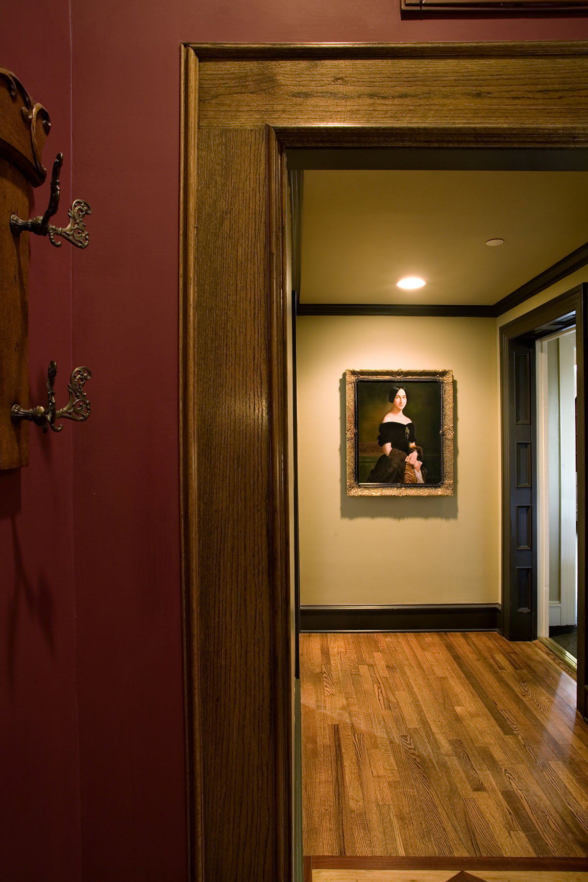 Rich wood trim and flooring is accented by a red painted wall and a large portrait painting of a woman in a black dress