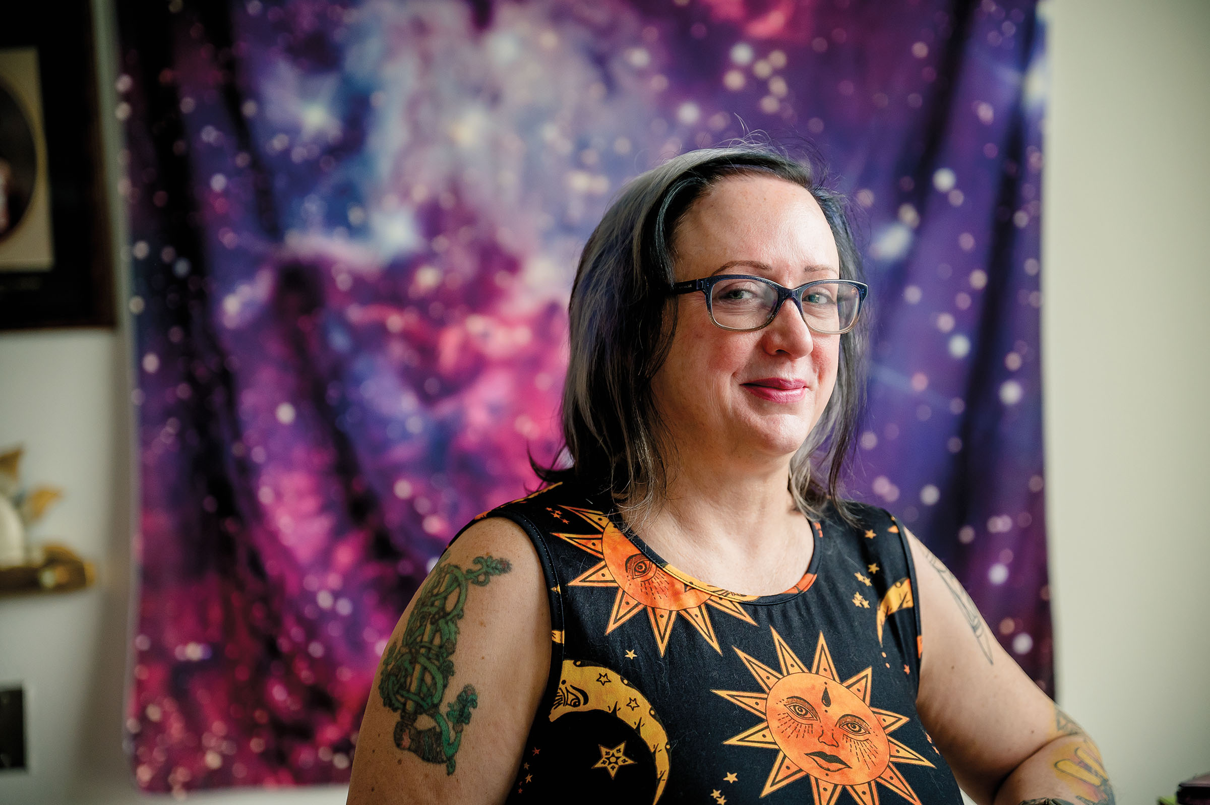 A woman in a sun and moon shirt stands in front of a large purple and stars-themed tapestry
