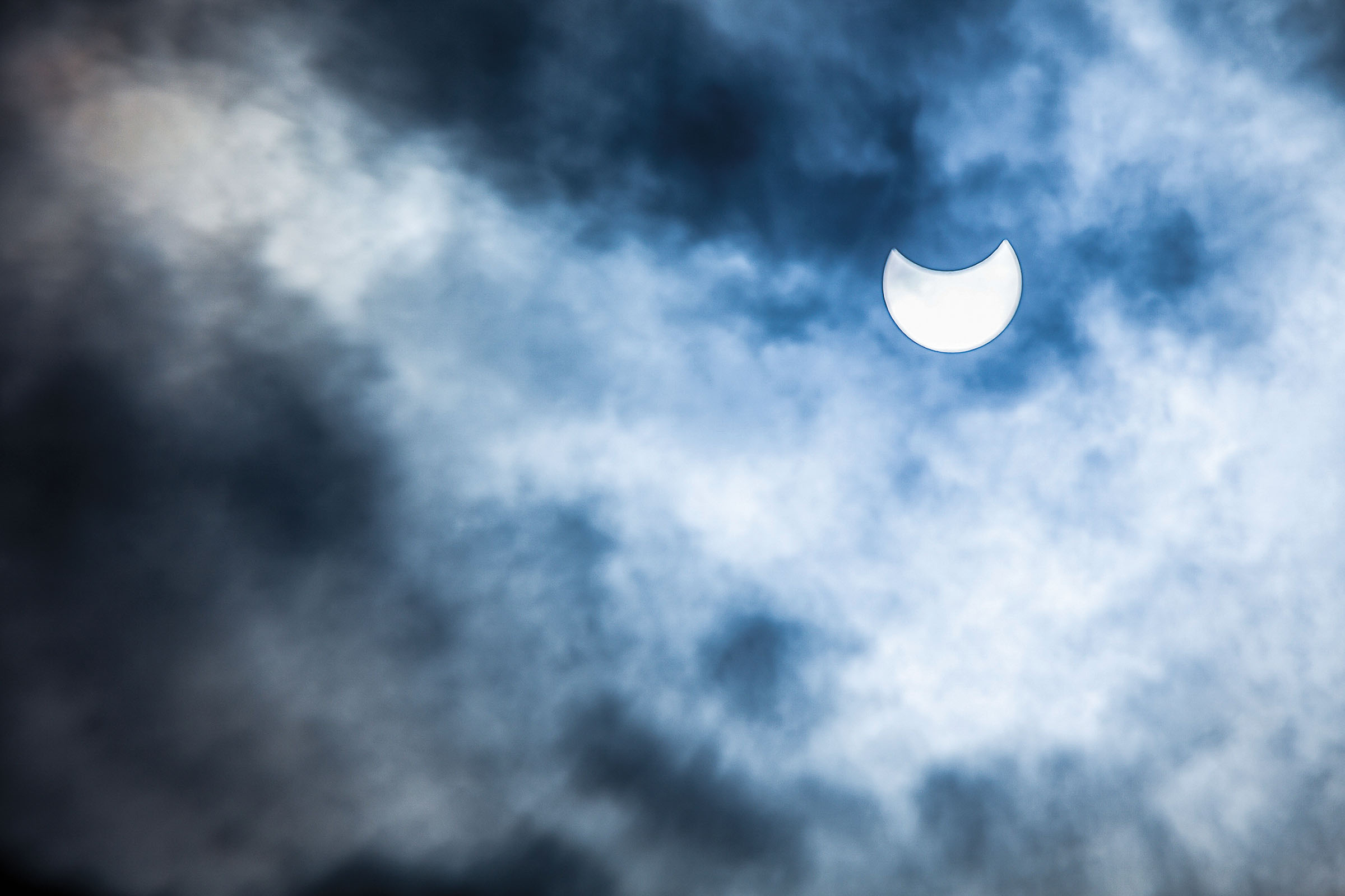 An eclipsed sun in a half-moon shape partially blocked by clouds