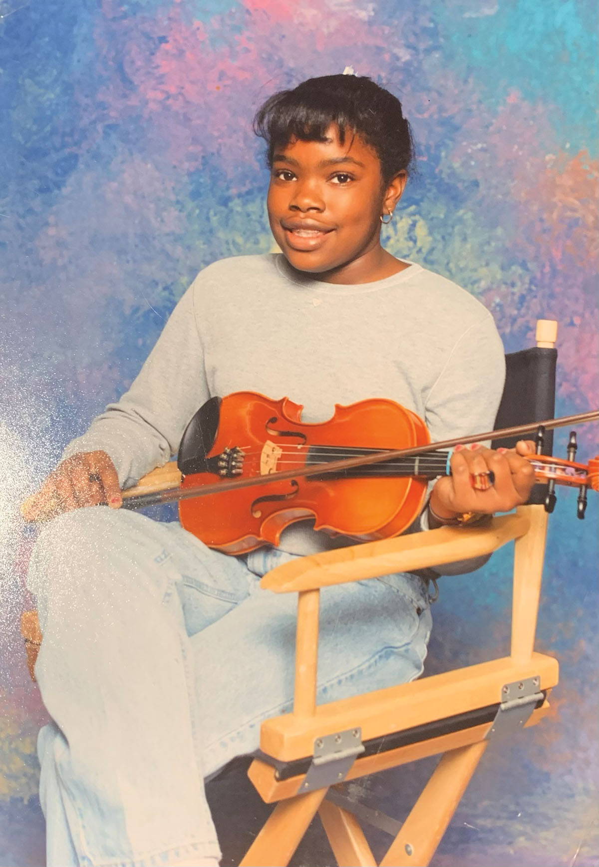 A young woman sits in a chair with a violin on a colorful background