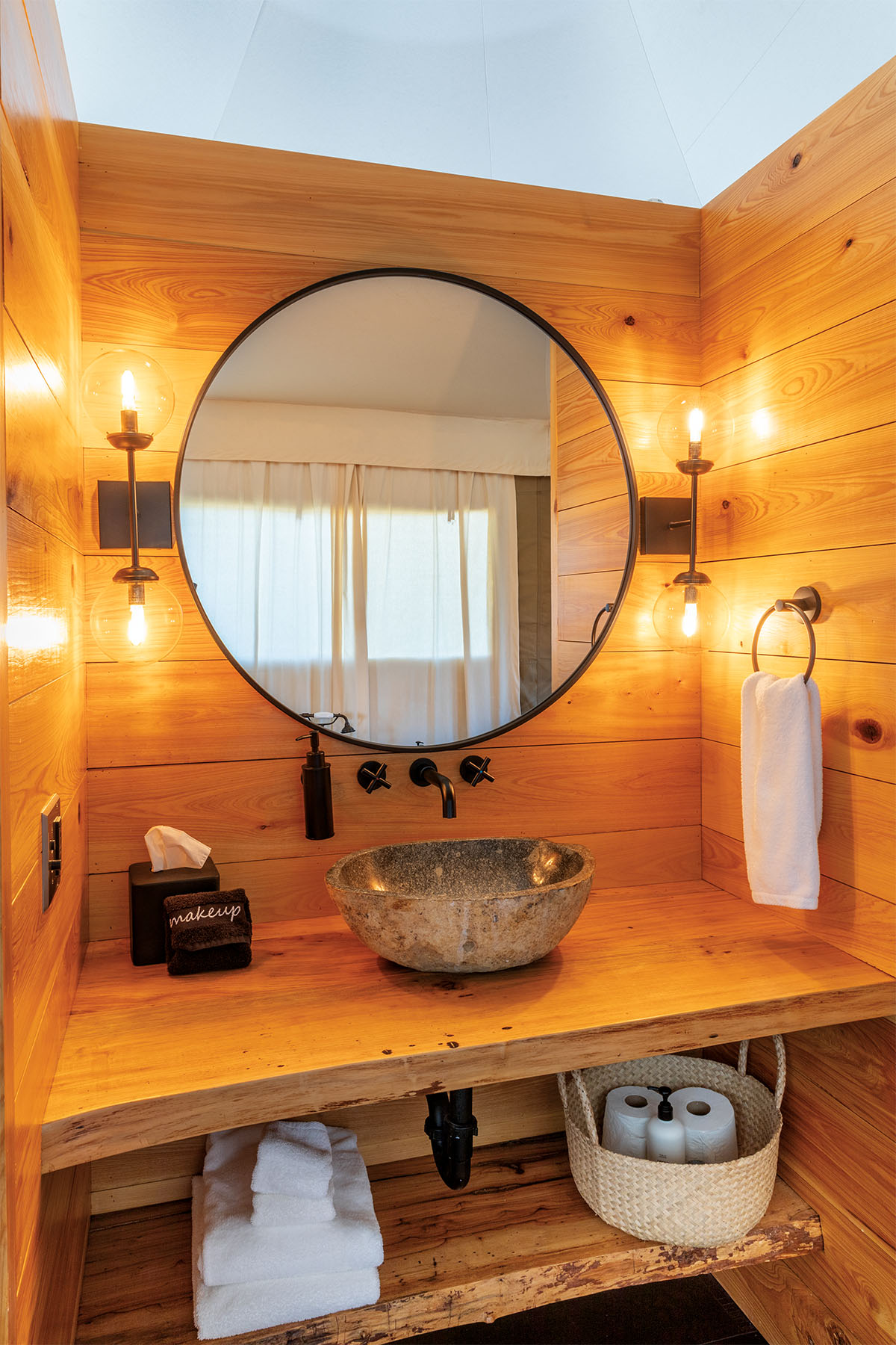 A circular mirror is illuminated by golden lights on a wood-paneled bathroom