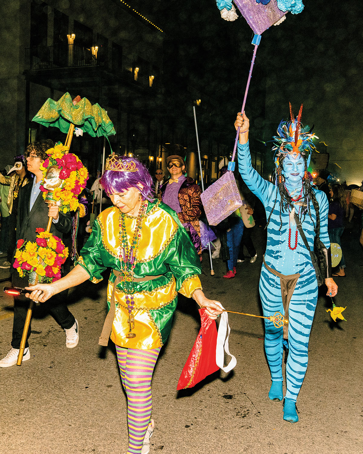 More people in costumes walking in a parade--including a bright green, gold and purple costume and one that is bright blue with animal stripes