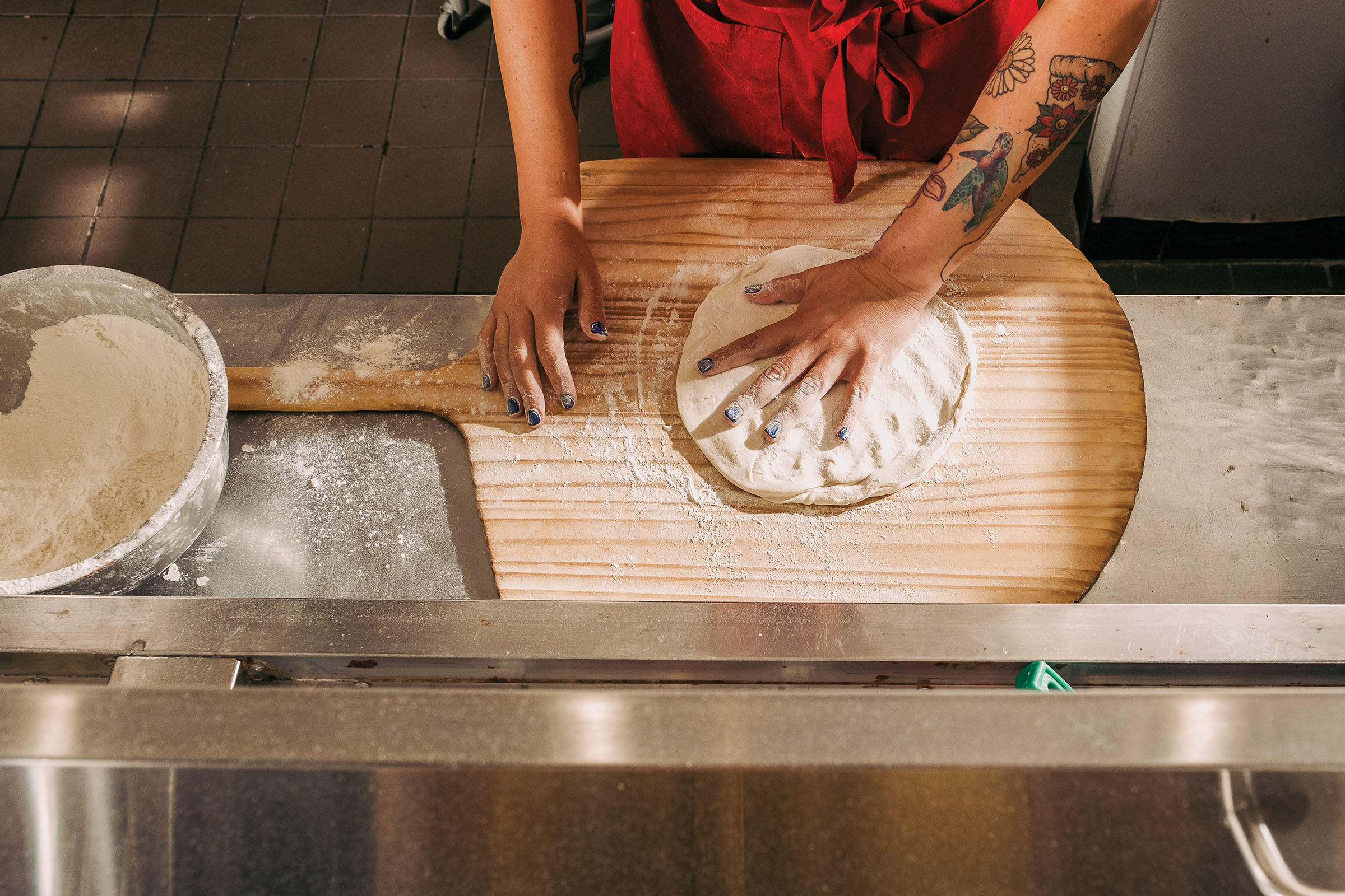 An overhead view of hands working with pizza dough on a wooden peel