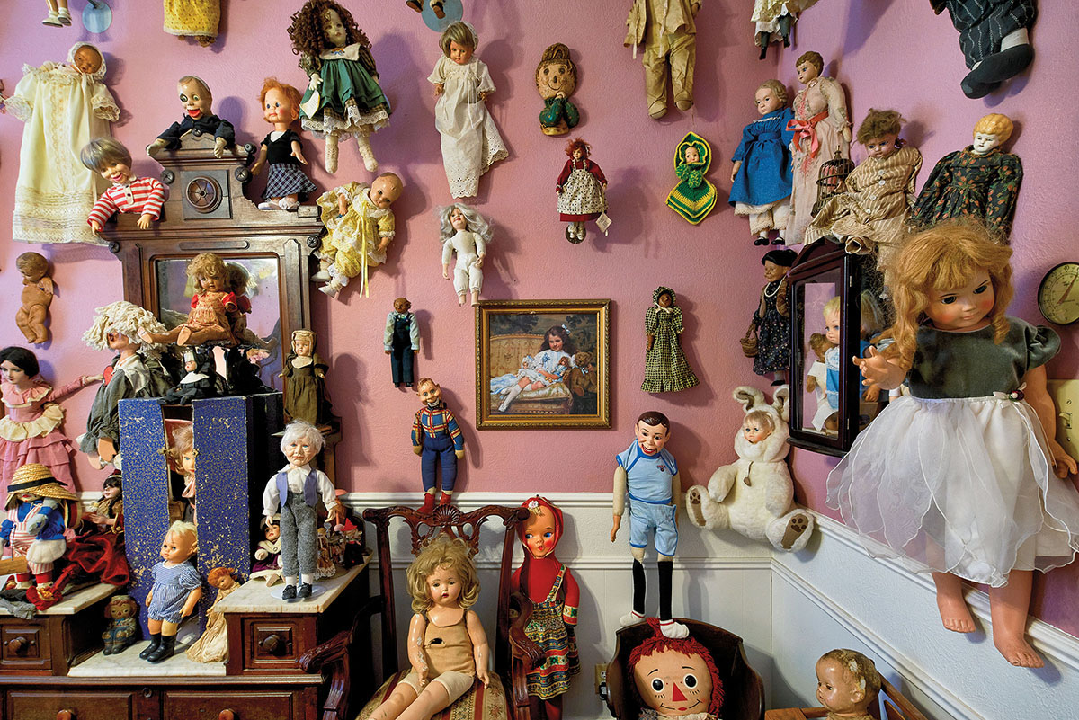 A collection of dolls mounted on a pink-painted wall
