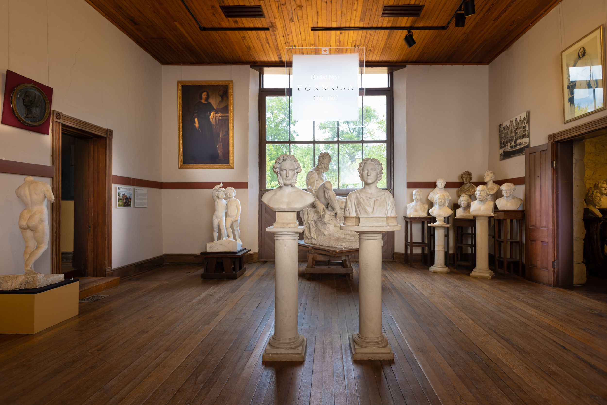 The main entrance of the museum shows two busts in foreground and other toward the back of the room, which has wood floors and a large window. A sign reading "Formosa" hangs in front of window. 