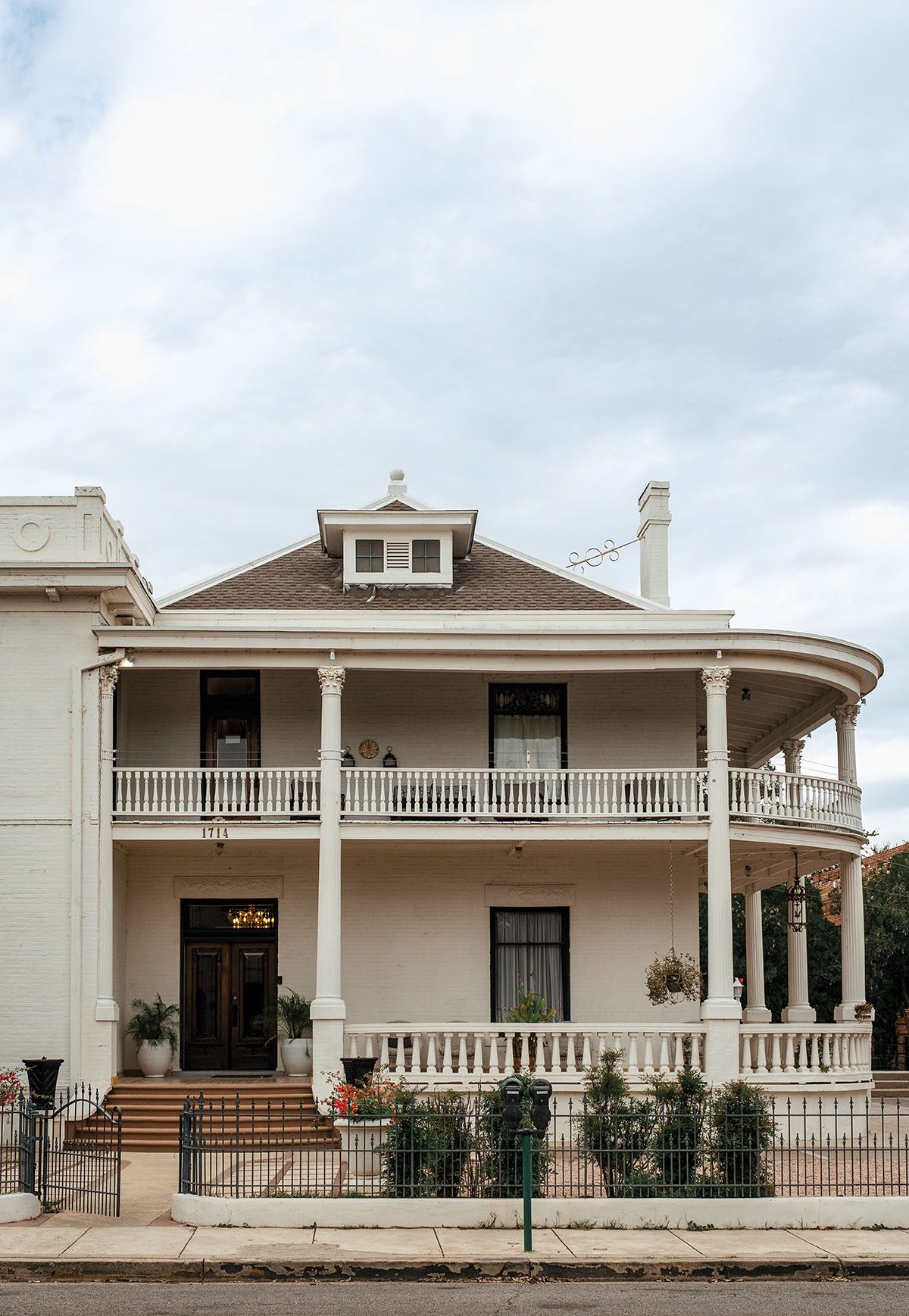 The exterior of a large mansion with a wraparound porch and white paint job