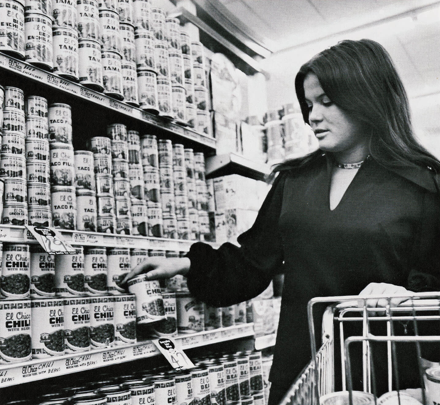 A black and white historic picture of a woman shopping for canned goods