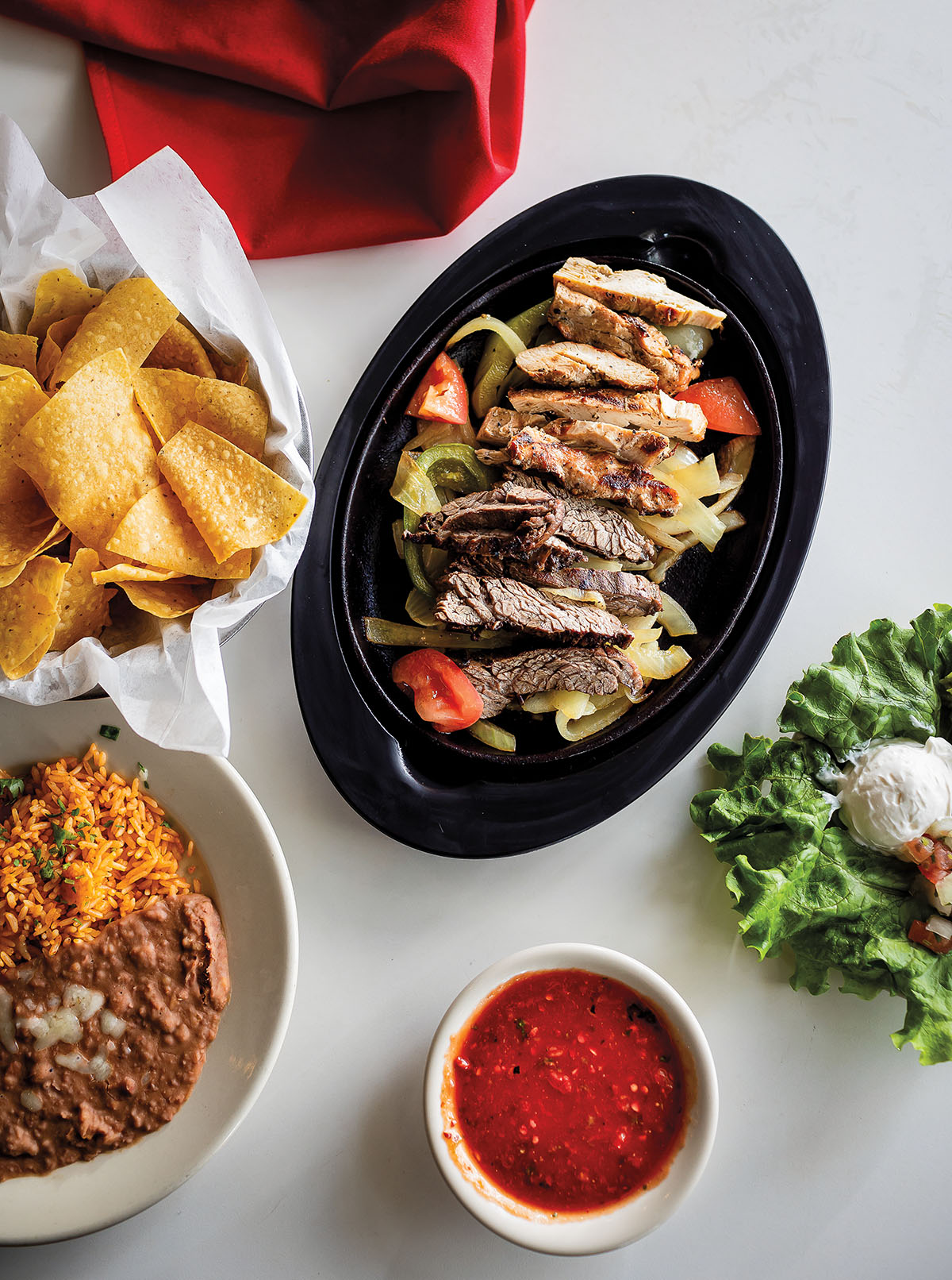 An overhead view of platters of fajitas, chips, salsa, and more