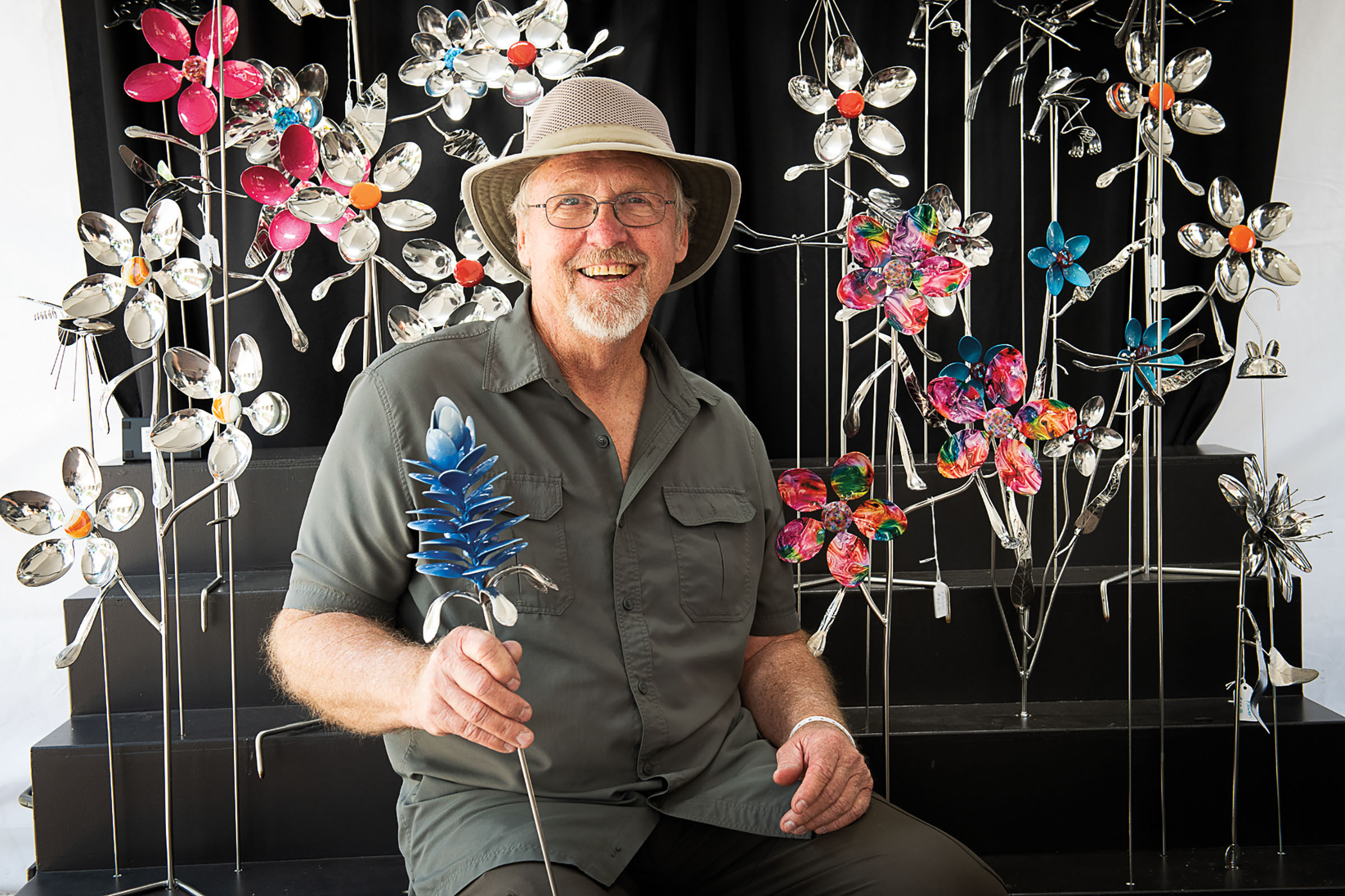 A man holds a metal bluebonnet in front of an array of other metal flowers on a dark background