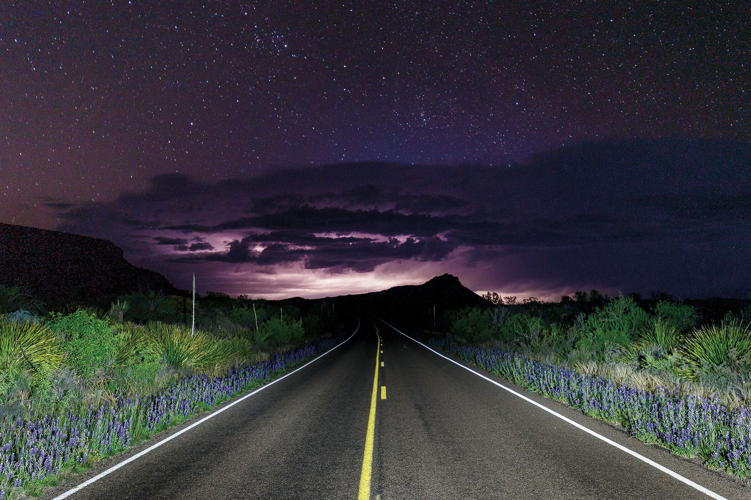 A lightning storm with dark purple clouds over a lonely highway
