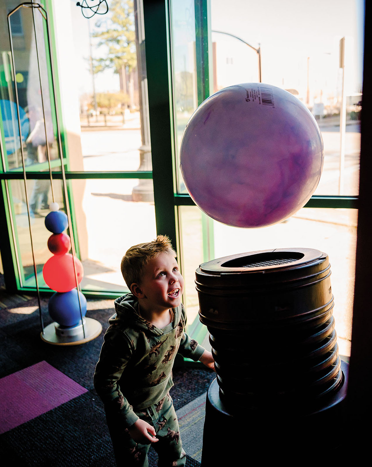 A young person watches as a large purple ball is held up by air above a large tube