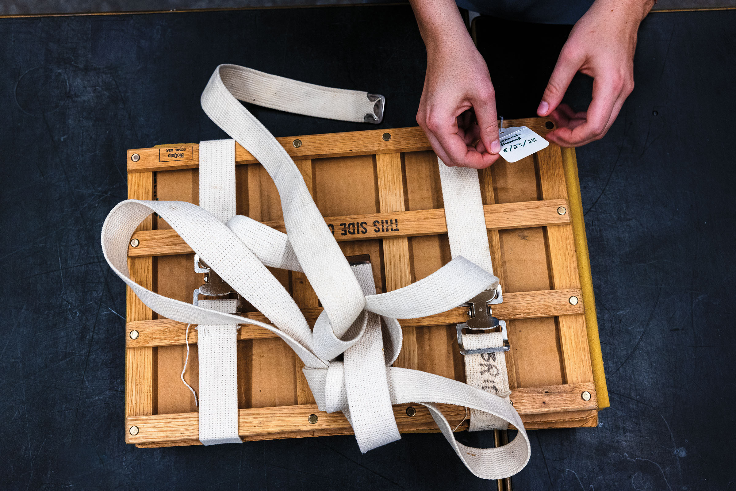 An overhead view of a person tightening white straps on a wooden pressing contraption