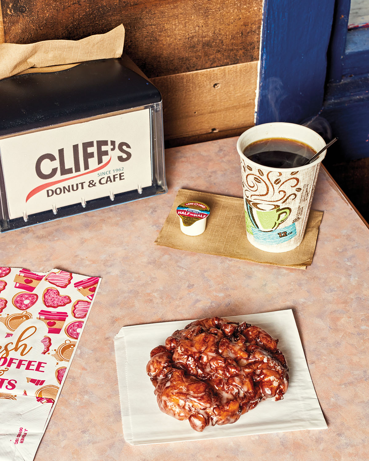 An overhead view of a golden apple fritter on a napkin next to a cup of coffee