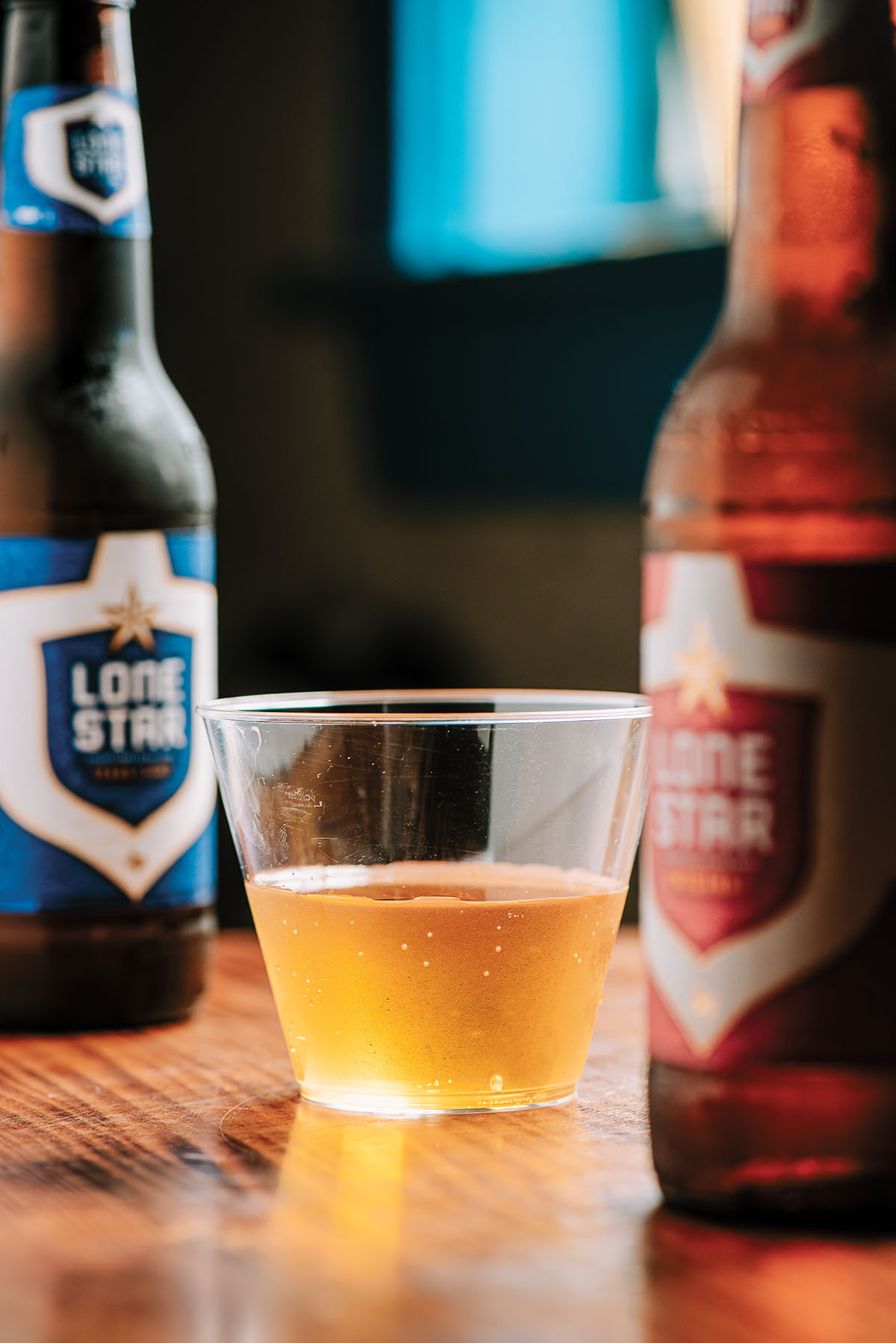 Two bottles of Lone Star beer stand next to a small cup filled with a golden brown liquid