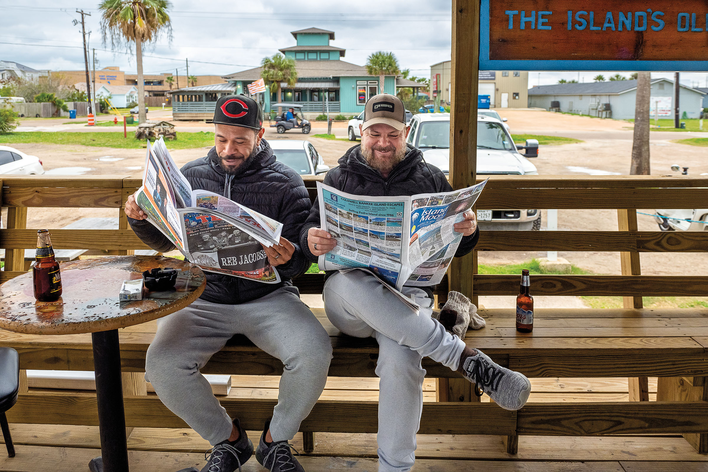 Two men sit on a wooden bench reading newspapers