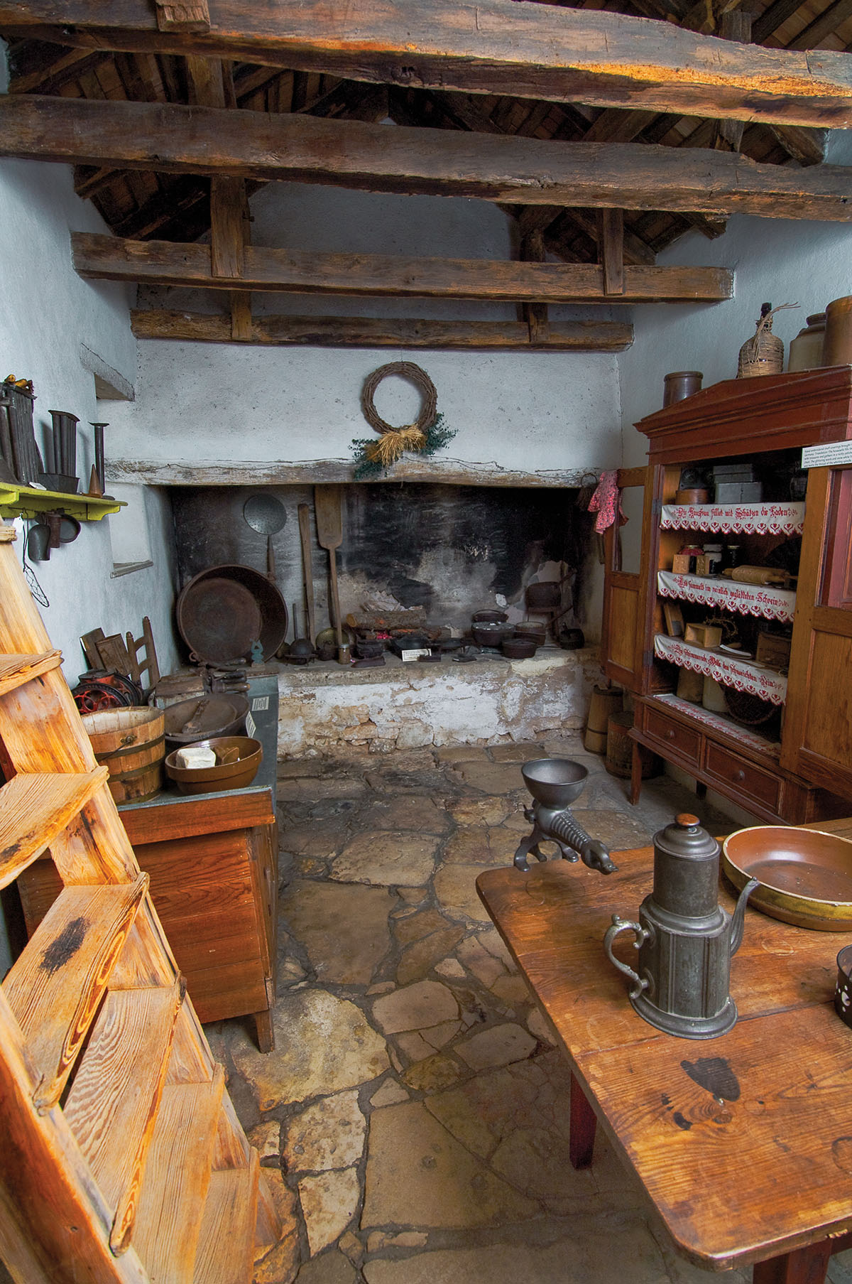 The interior of a room filled with numerous artifacts including cooking items, a ladder, and a stone floor