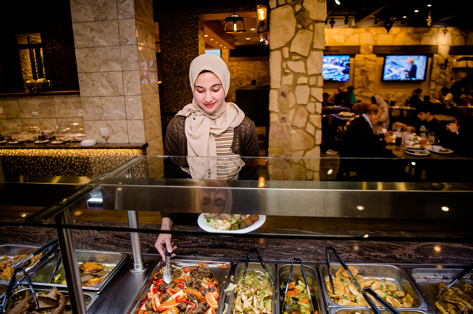 A woman dressed in a hijab serves a plate of food at a buffet
