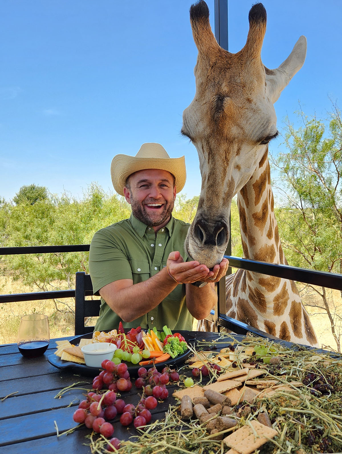 A picture of a man eating a fruit plate and sharing with a giraffe