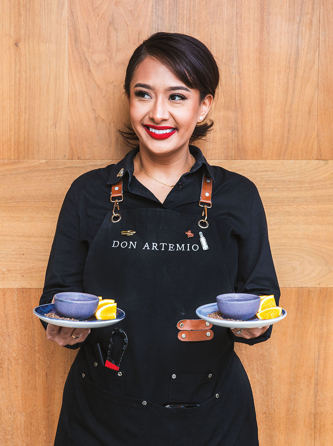 A person wearing a dark apron holds two plates with colorful bowls atop